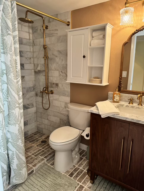Compact bathroom with shower, toilet, sink vanity, and white wall cabinet on beige and gray tile.