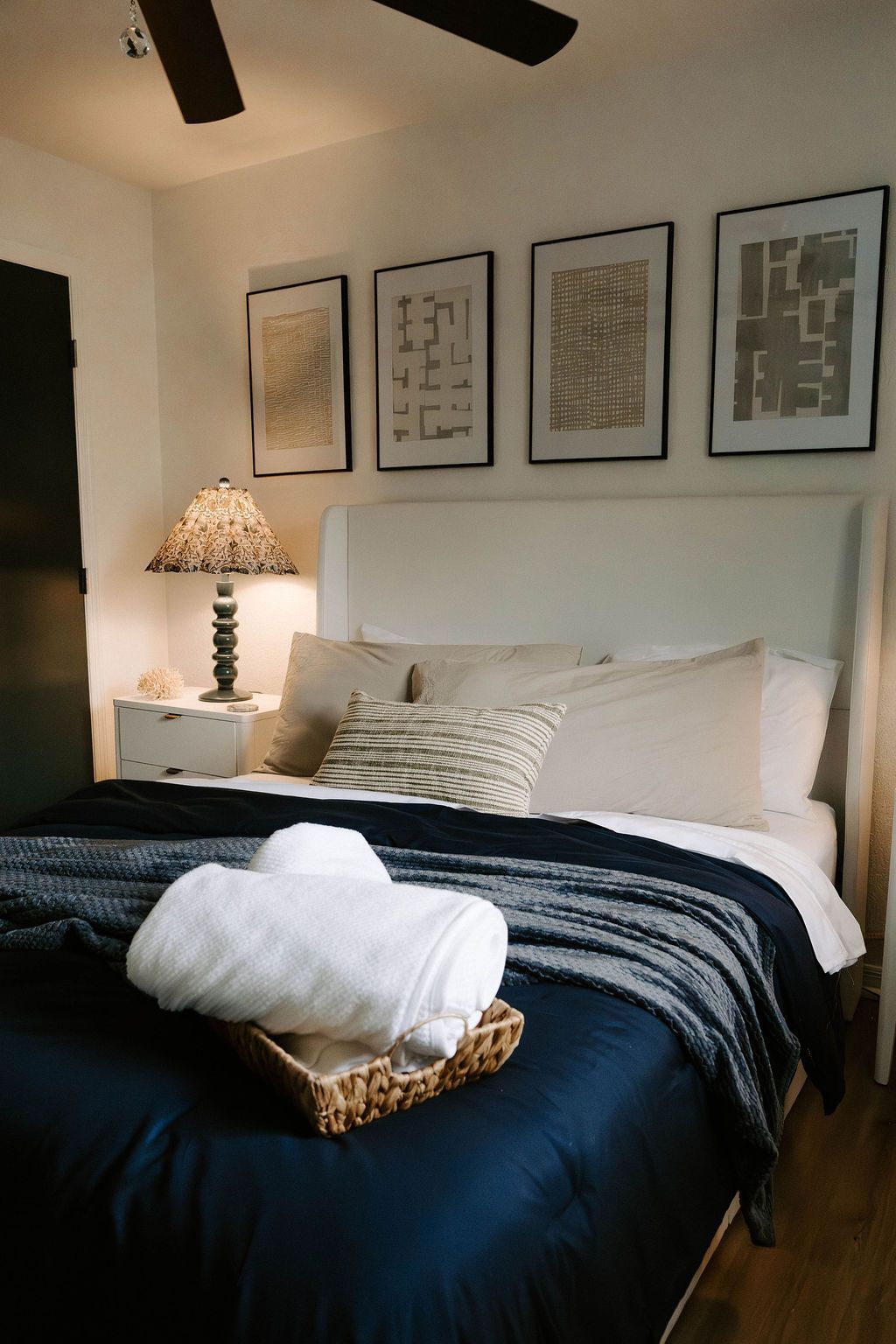 Cozy bedroom with a navy bedspread, white pillows, bedside lamp, and four framed prints above the headboard