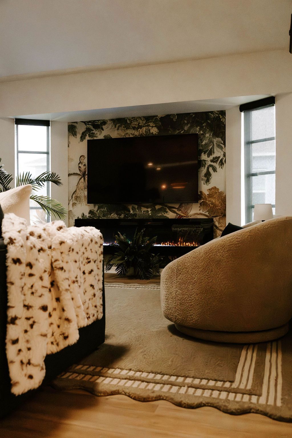 Cozy living room with wall-mounted TV, floral armchair, beige chair, and striped rug