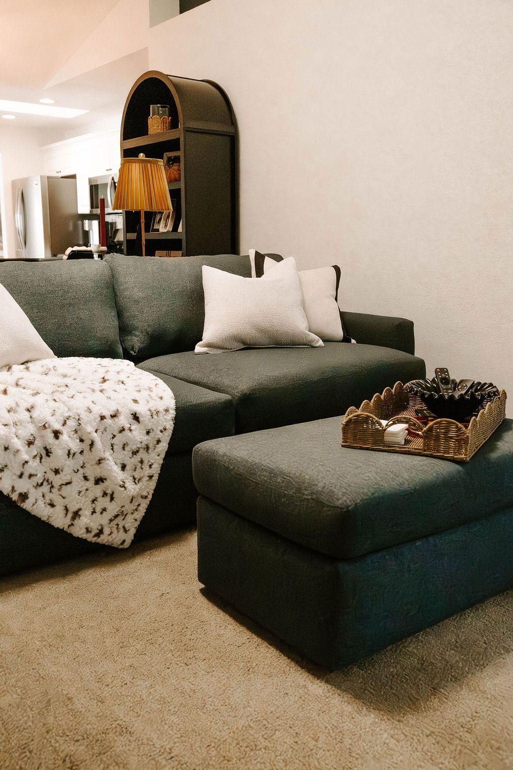 Gray sectional sofa with white pillows, ottoman tray, and patterned throw in a cozy living room.