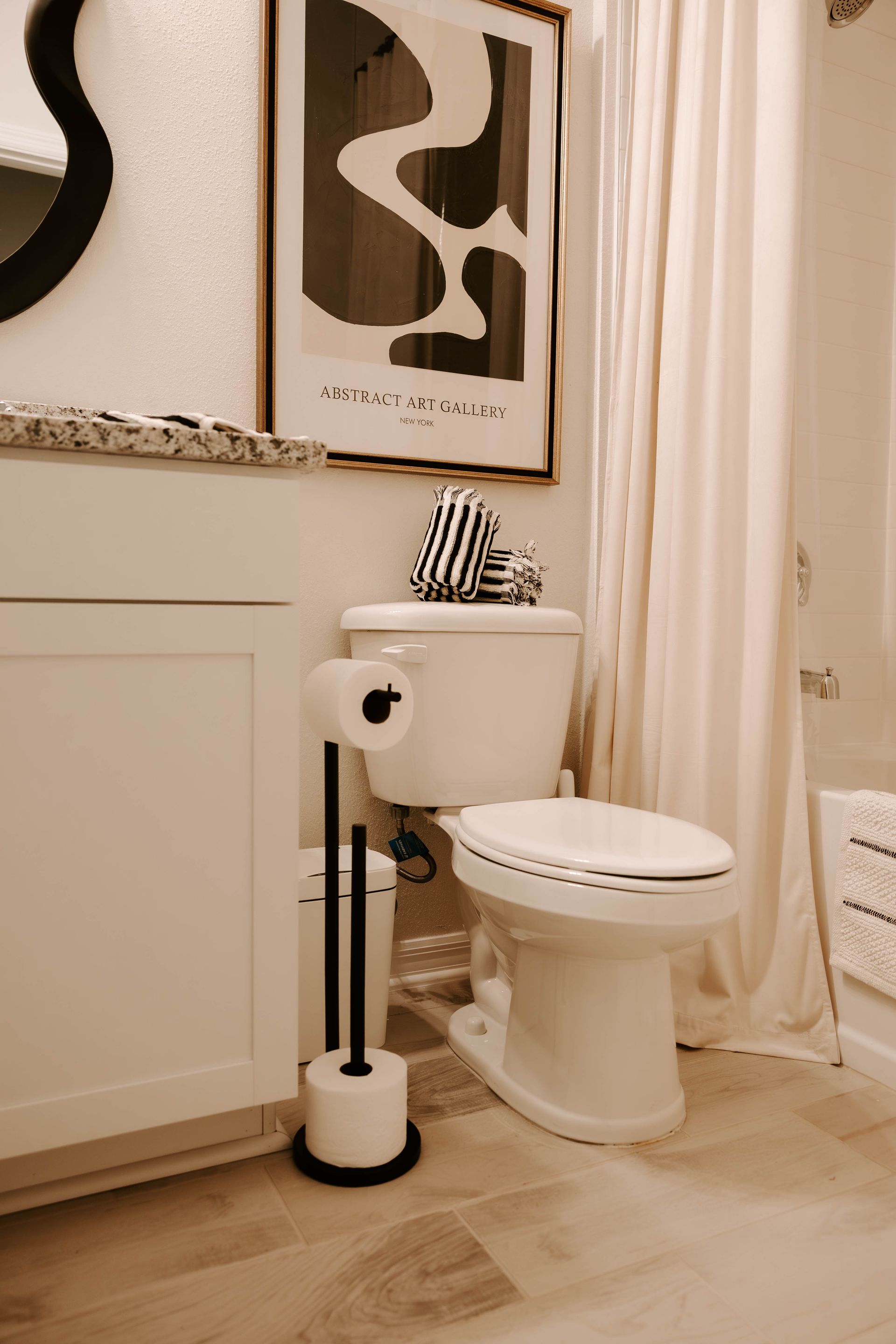 Small beige bathroom with a toilet, toilet brush, wall art, and a shower curtain.