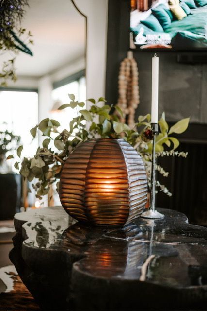 Amber ribbed glass vase with greenery on a reflective black tabletop in a cozy living room