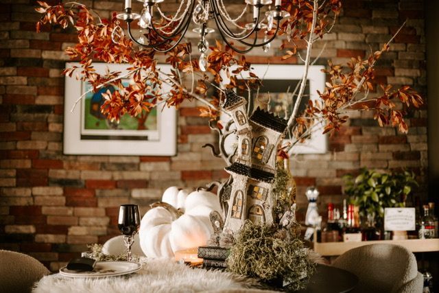 Autumn table display with pumpkins, candles, and a leafy centerpiece against a brick wall