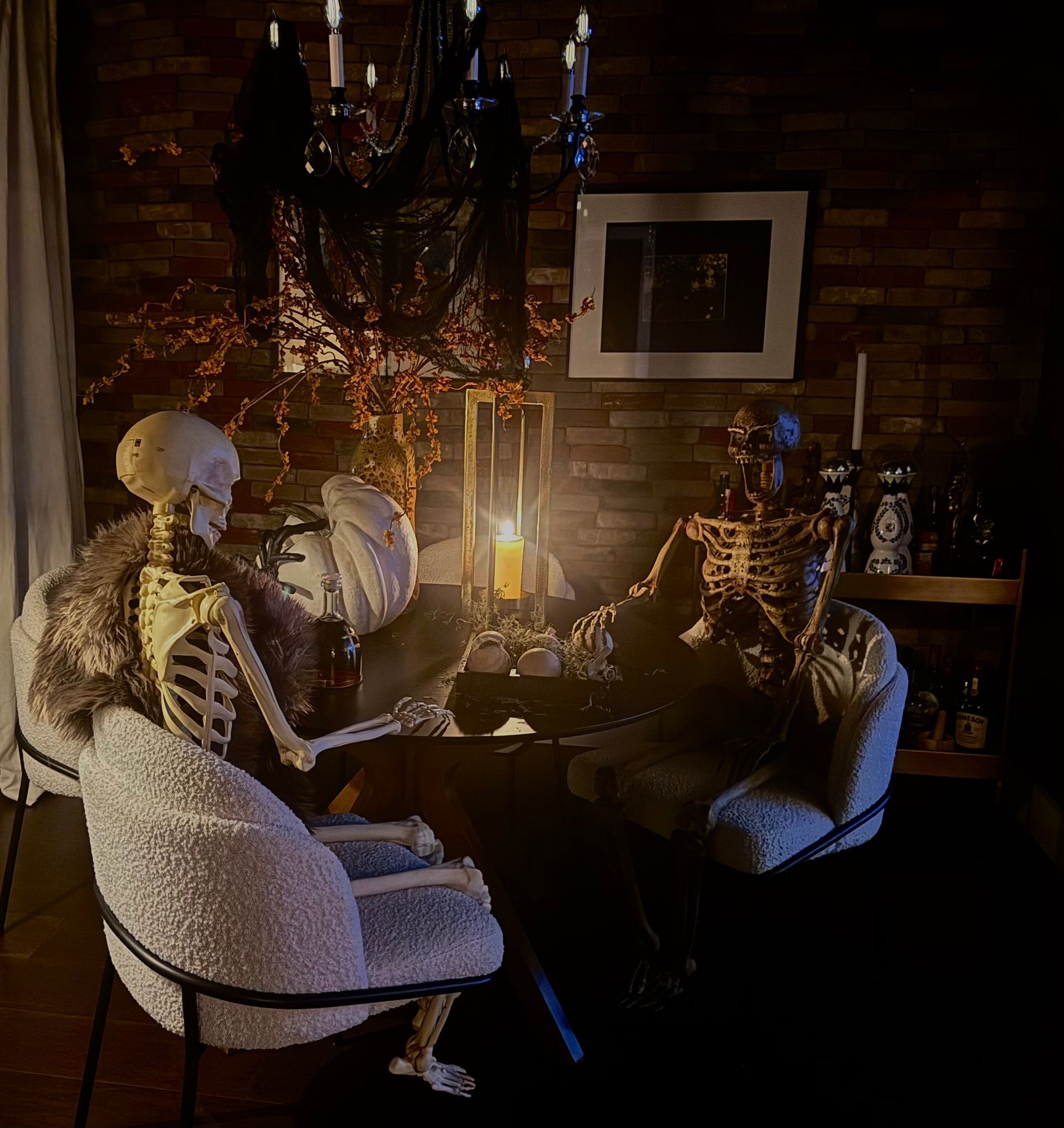 Skeletons gathered around a candlelit table in a dark room with chandeliers and brick walls