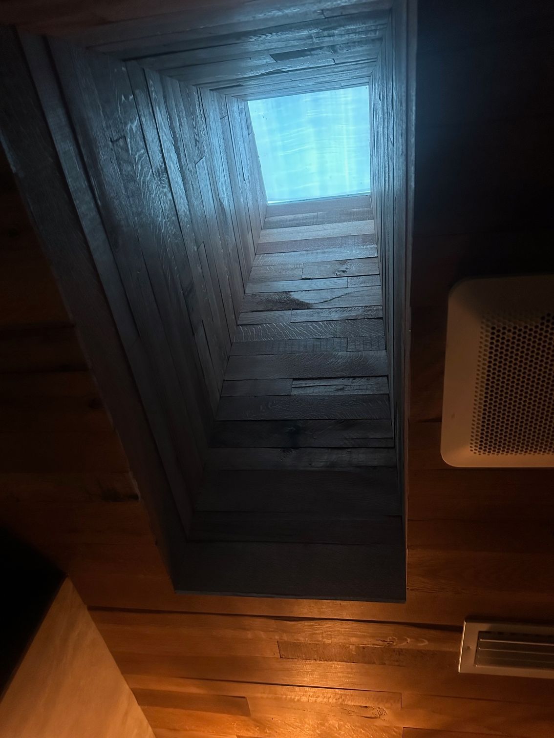 Dimly lit wooden ceiling with a rectangular skylight and a small vent or speaker on the right.