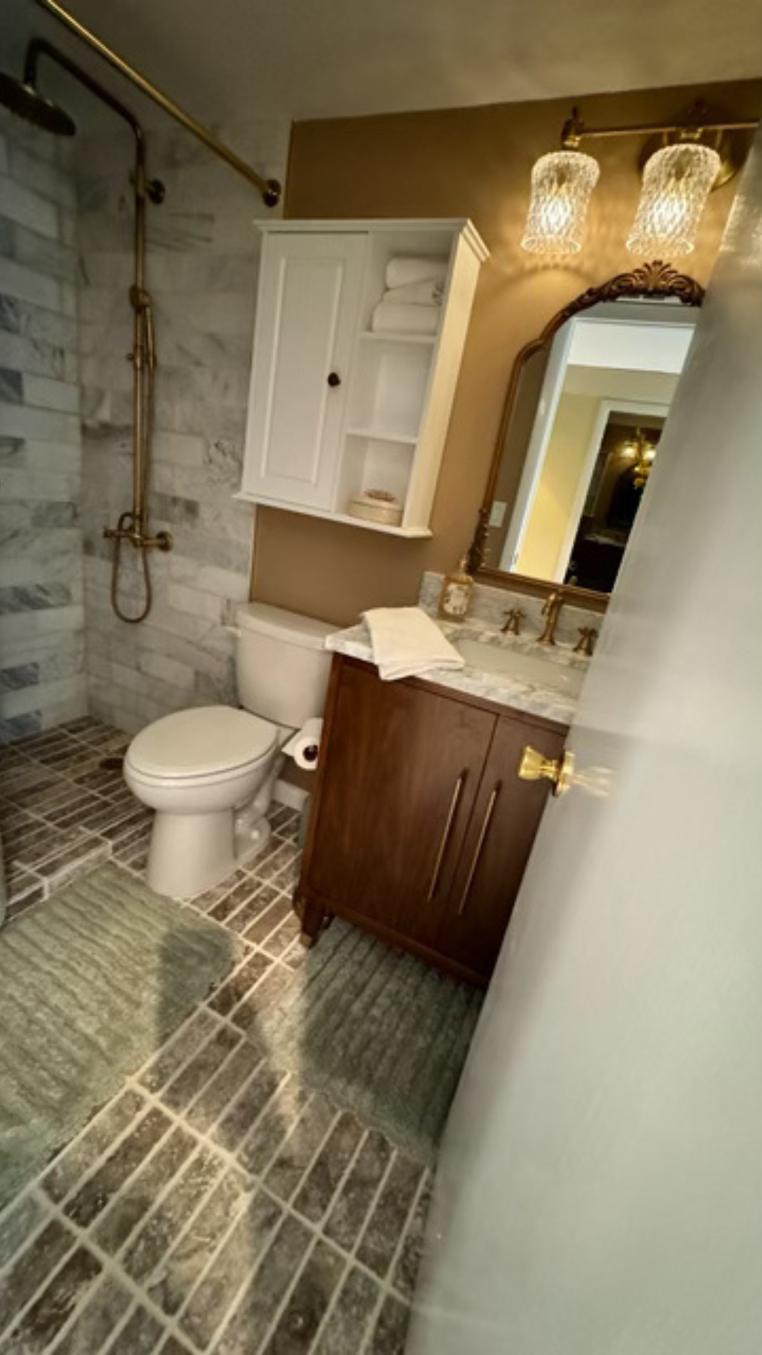 Small bathroom with walk-in shower, toilet, vanity, mirror, and patterned tile flooring.
