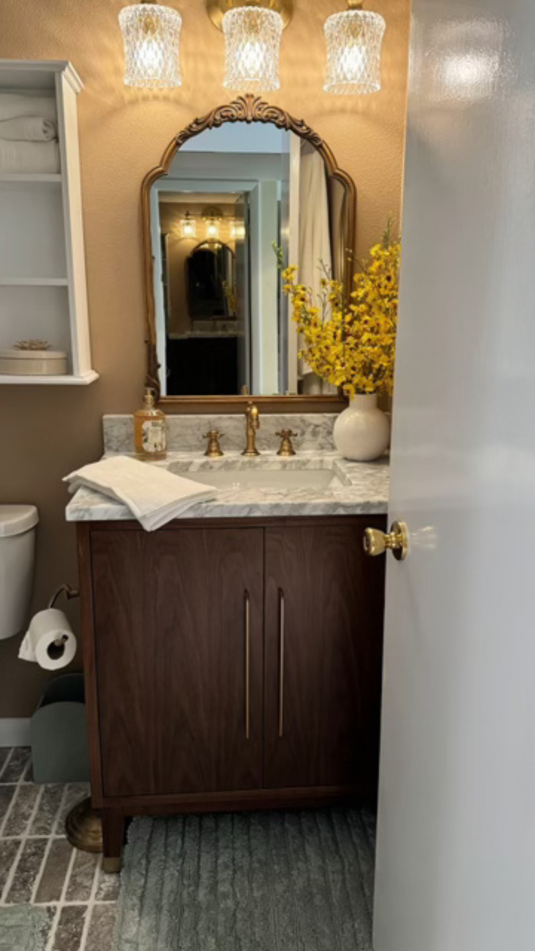 Small bathroom vanity with mirror, warm lights, marble sink, dark wood cabinet, and open book on the counter.