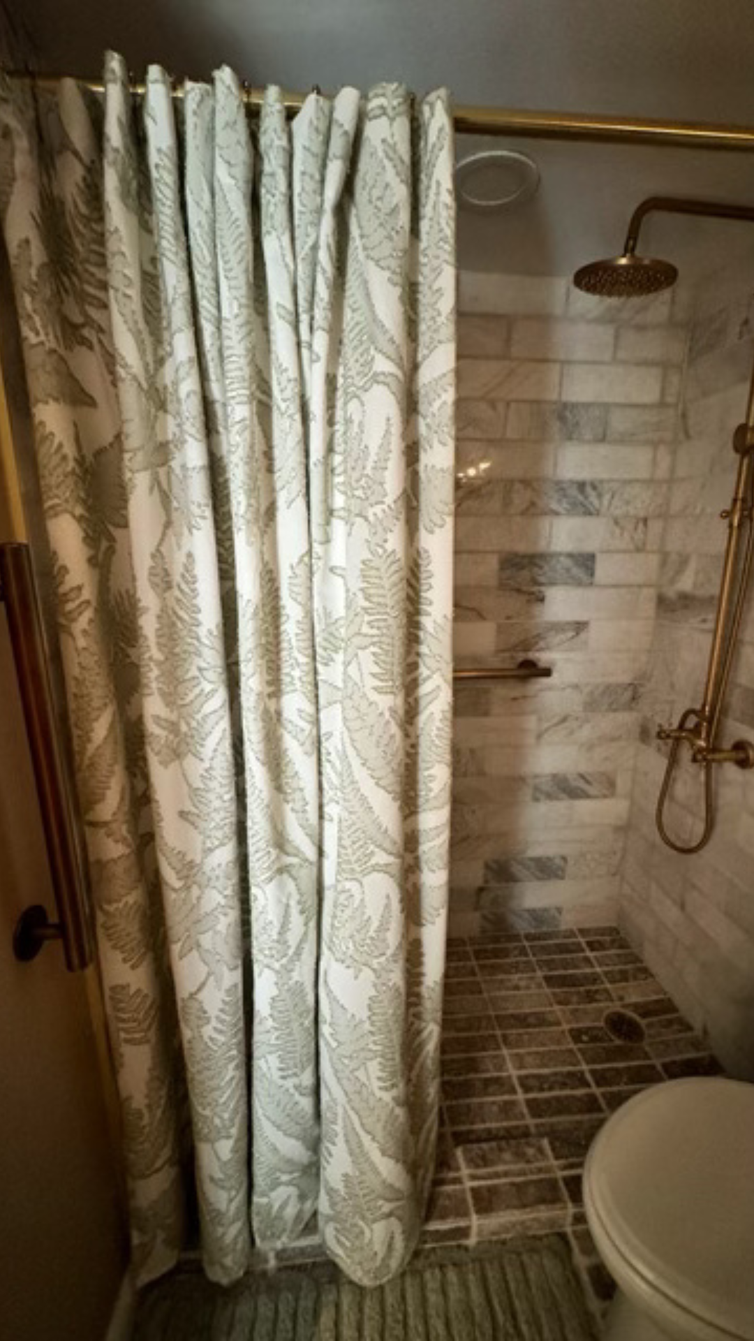 Small tiled shower with cream curtain, wall-mounted showerhead, and partial toilet visible.