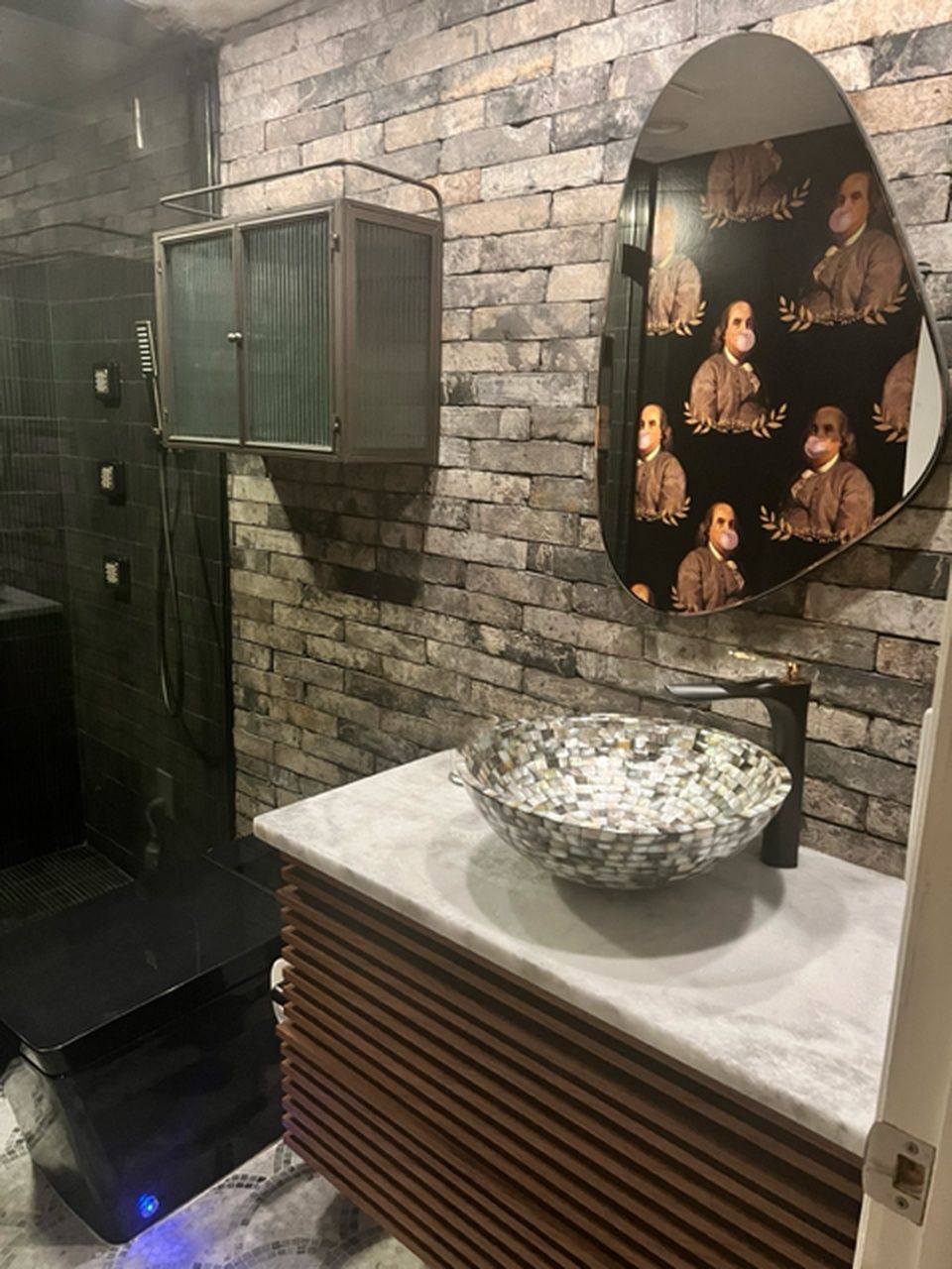 Stone-tiled bathroom vanity with round mirror, marble sink, and framed portrait on the wall