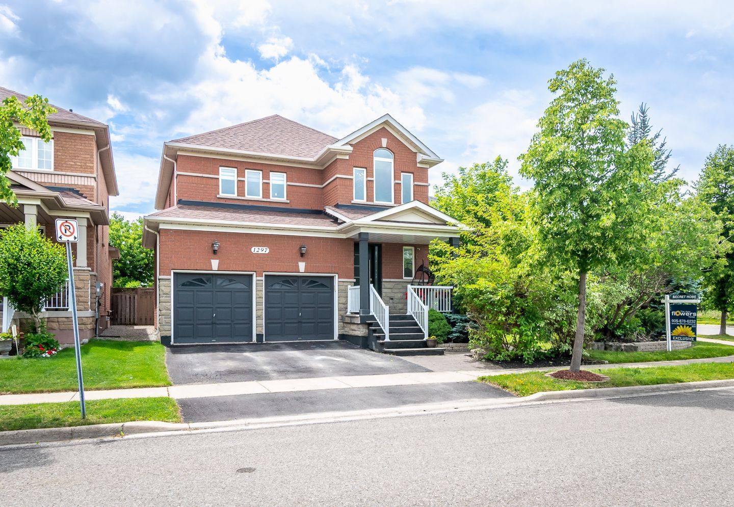 Brick two-story suburban house with a double garage, driveway, and trees lining the front yard.