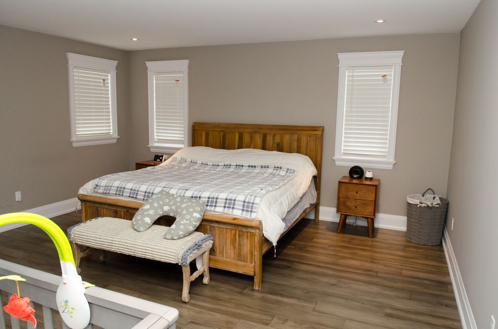 Bedroom with wooden bed, gray walls, white blinds, bench at foot of bed, and small nightstand.