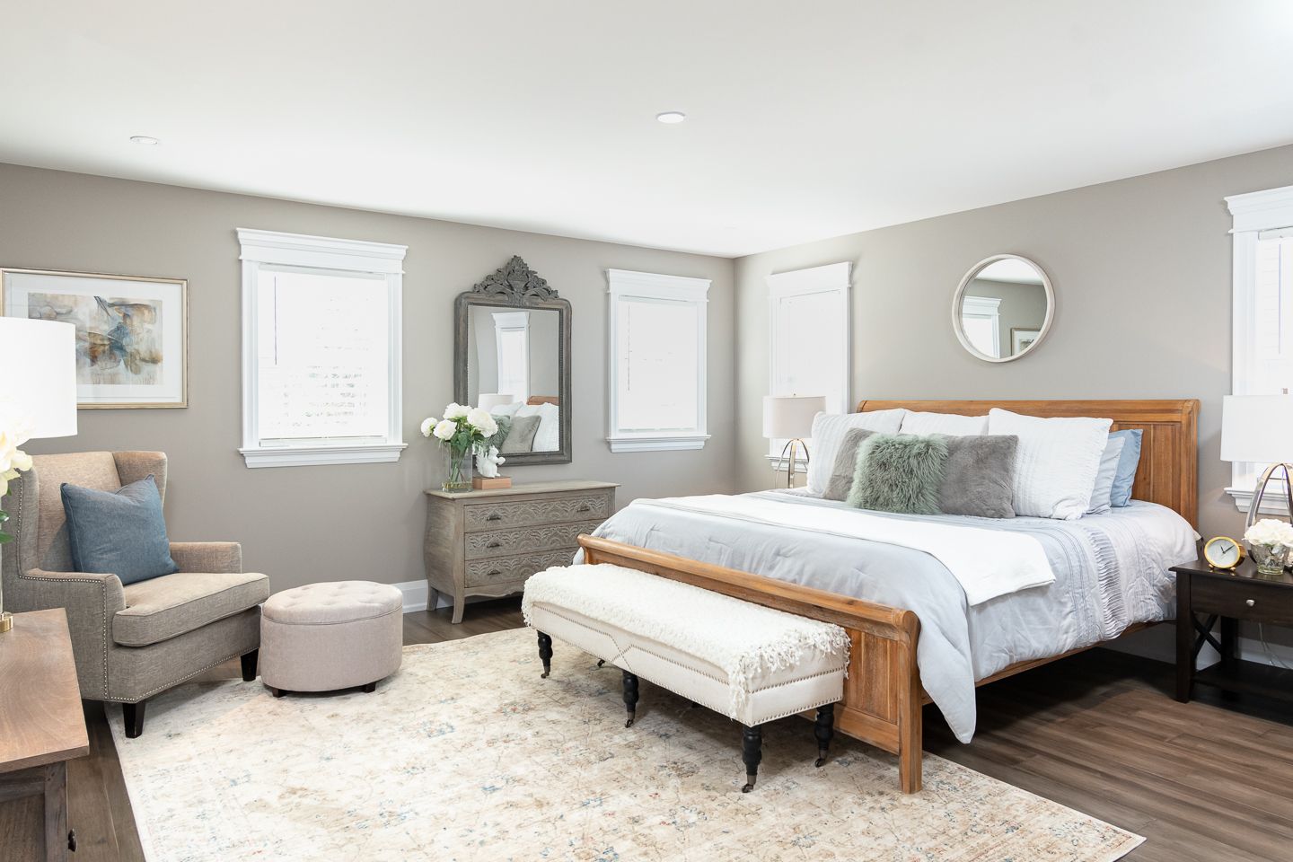 Bright bedroom with a wooden bed, gray armchair, side tables, and soft neutral decor