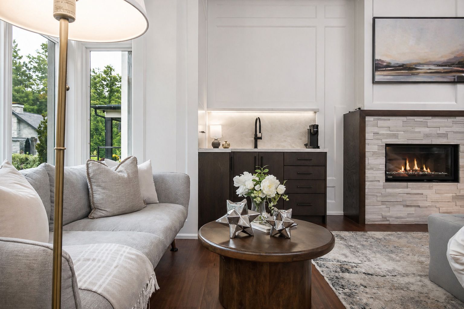 Bright modern living room with a gray sofa, round coffee table, fireplace, and built-in bar area