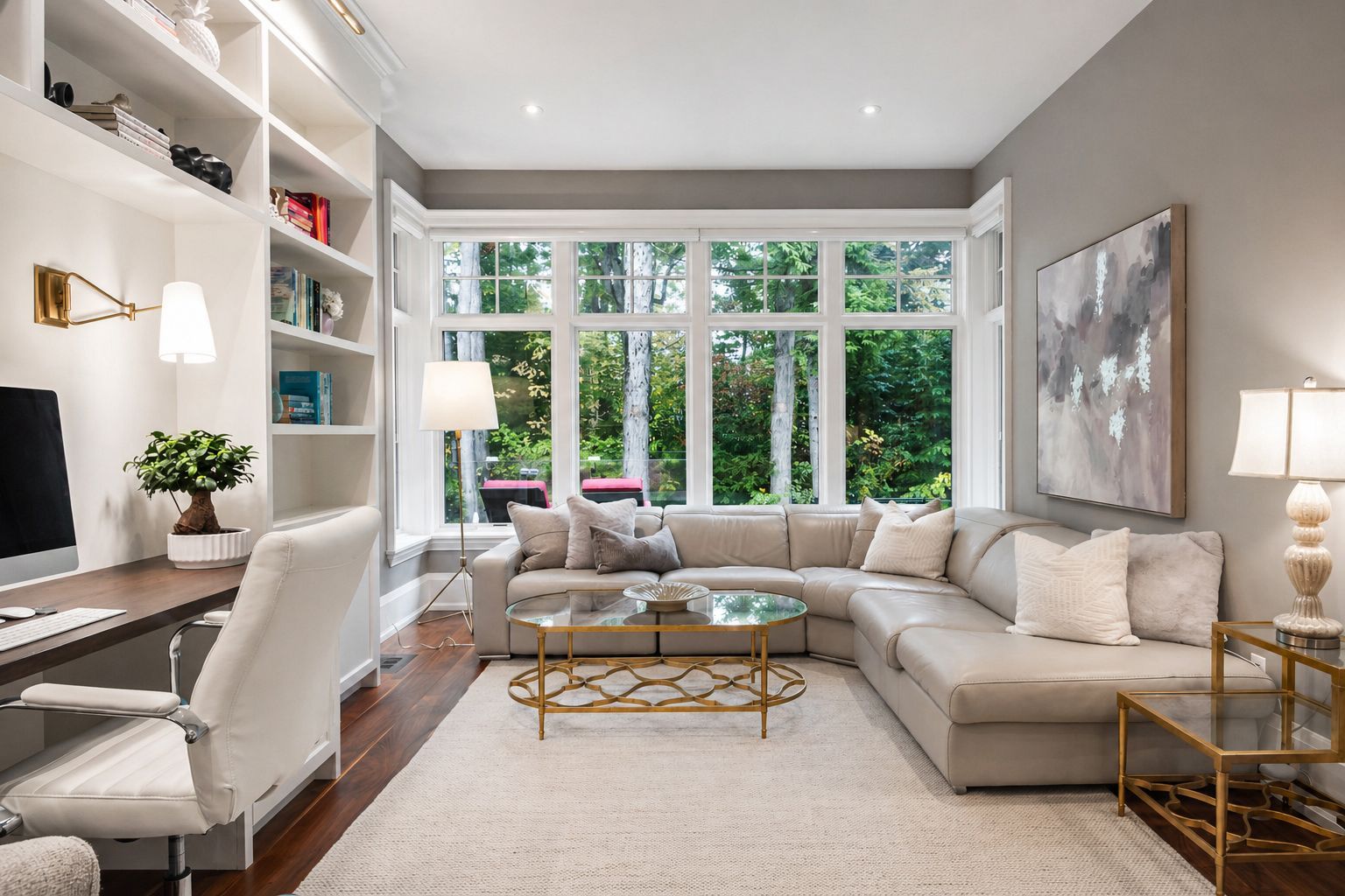 Bright modern living room with beige sectional, white desk chair, built-in shelves, and large windows overlooking greenery