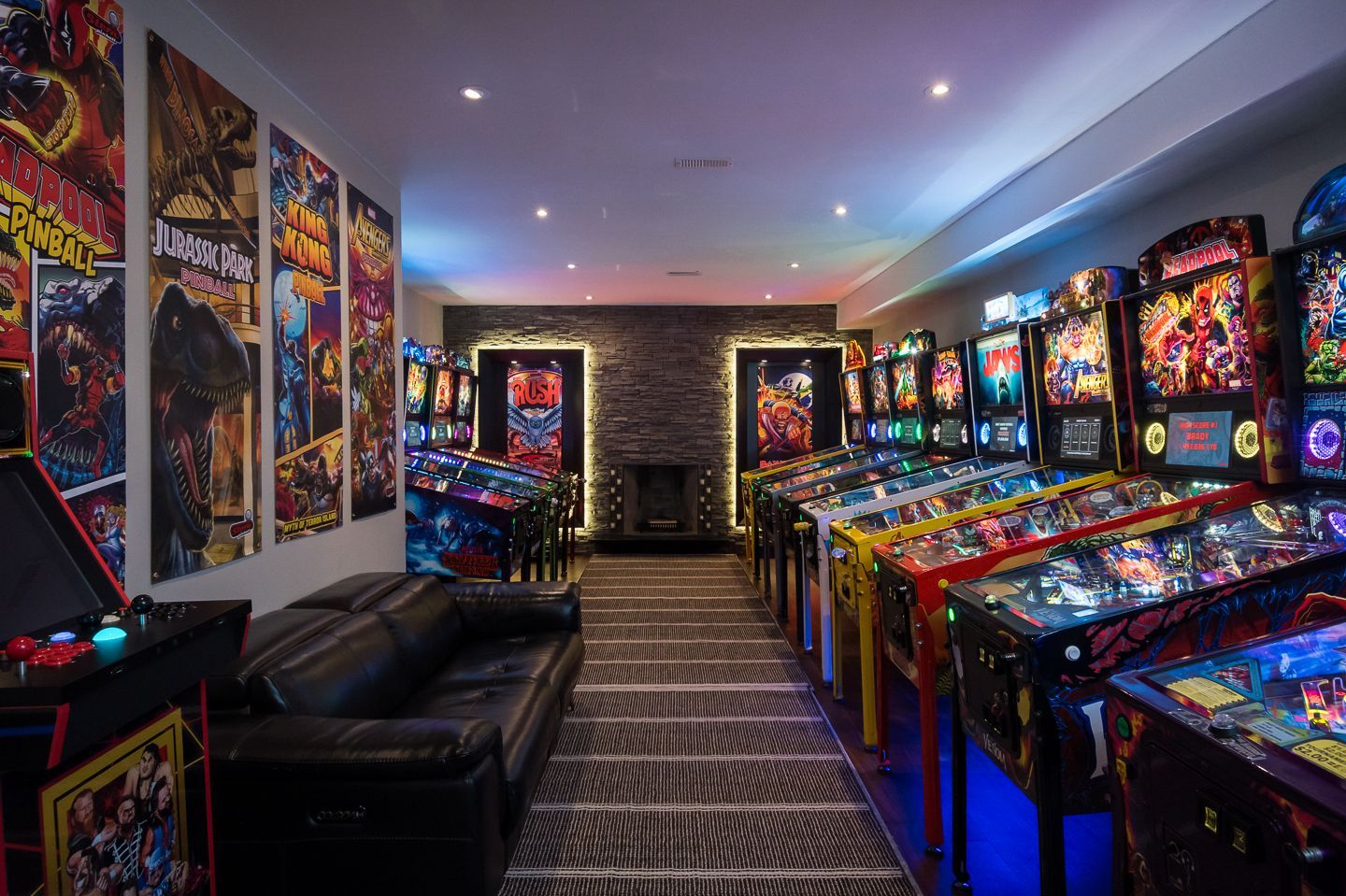 Colorful pinball arcade room with rows of machines, blue lighting, and a black couch along the wall