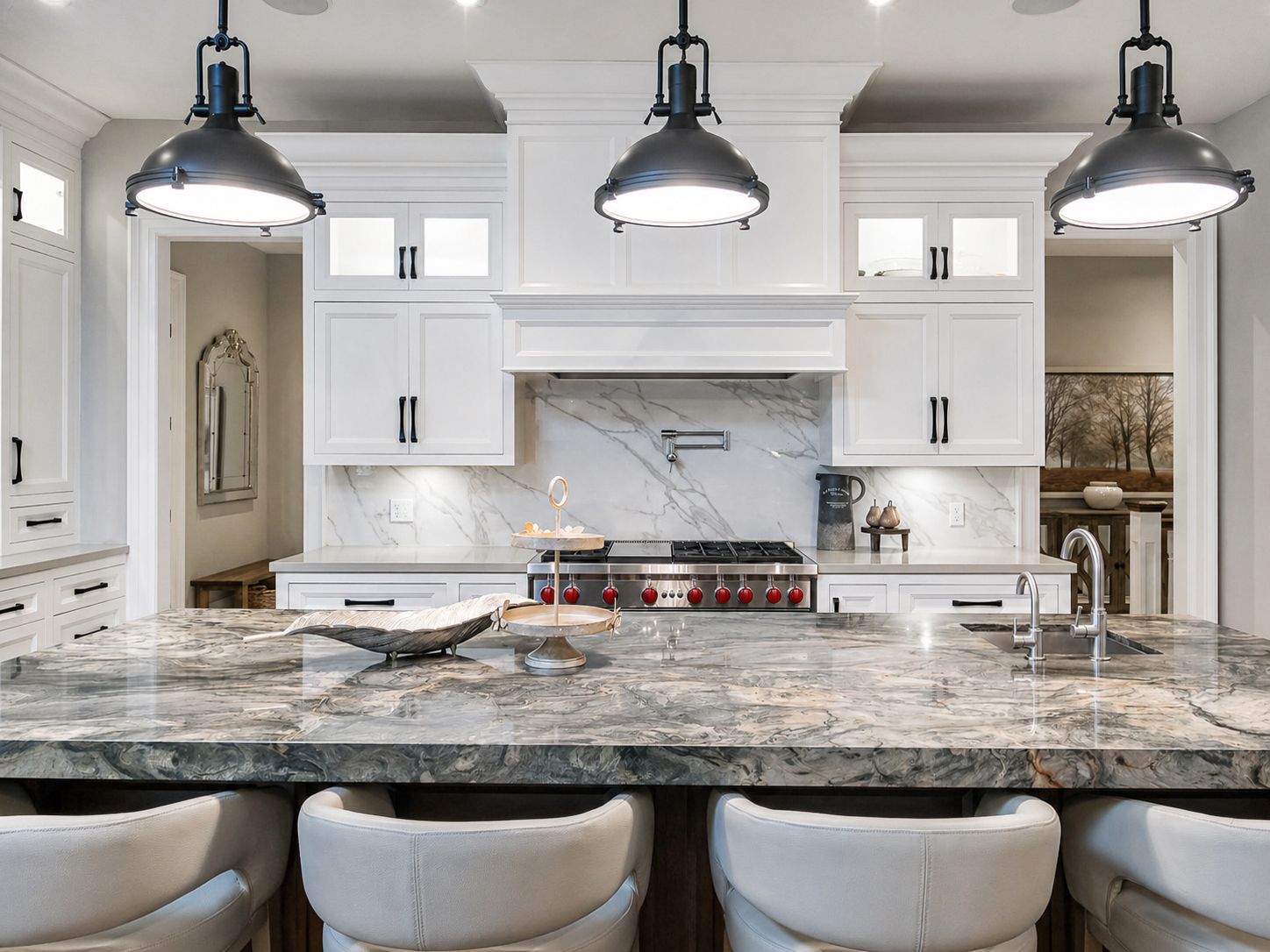 Bright modern kitchen with marble island, three pendant lights, white cabinets, and bar stools