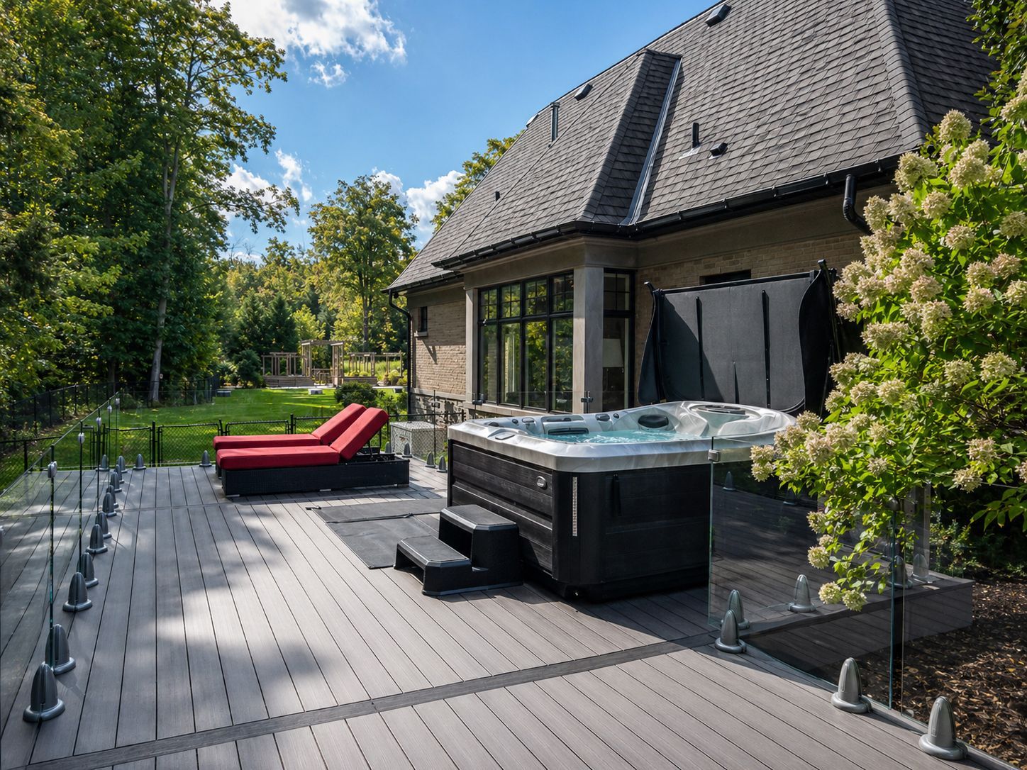 Modern patio with hot tub, red lounge chair, and a house beside a tree-lined garden