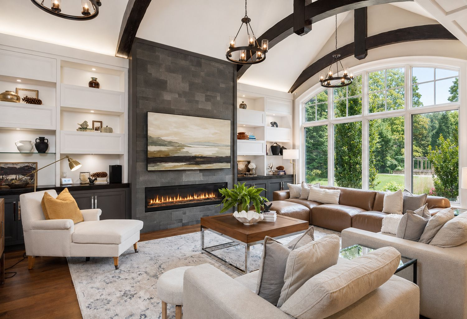 Bright modern living room with large windows, white sofas, leather ottoman, and neutral decor