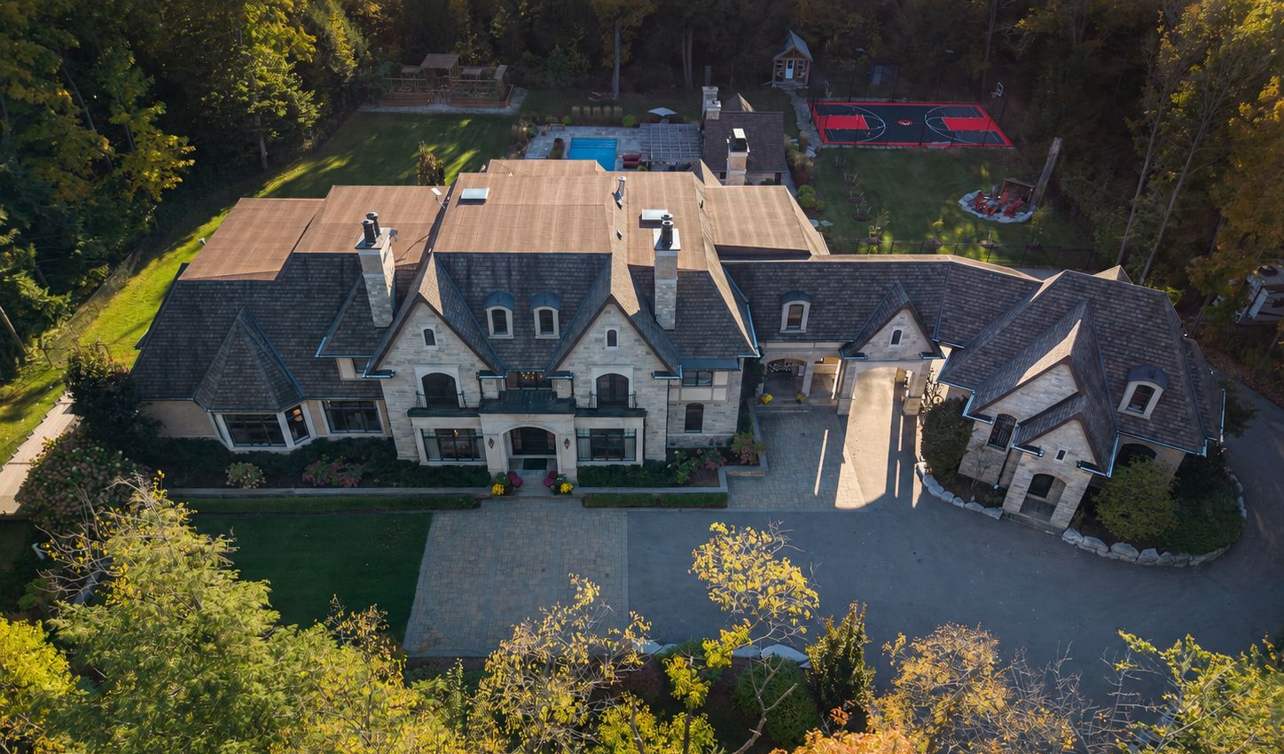 Aerial view of a large stone mansion with a circular driveway and trees surrounding it
