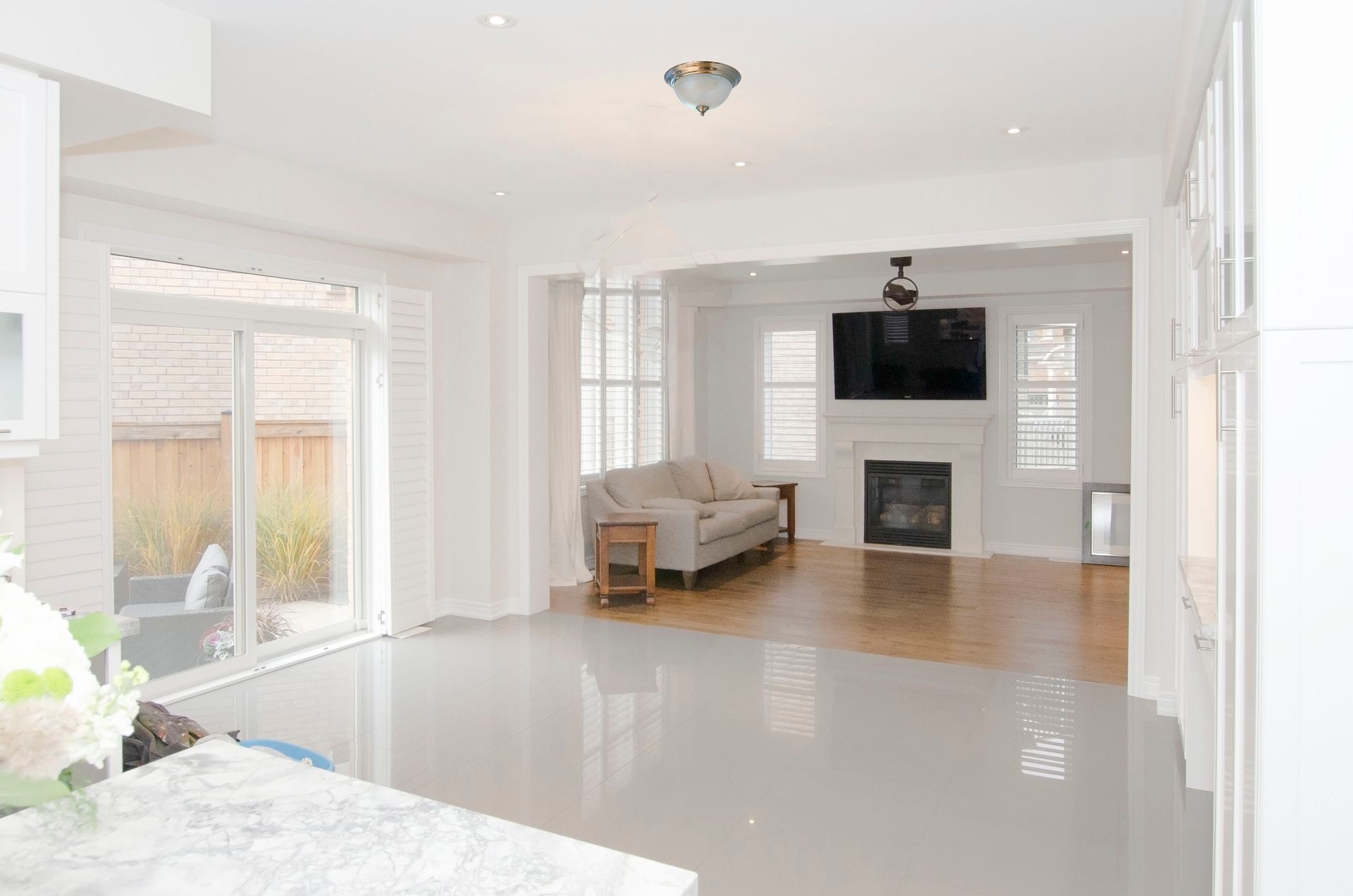 Bright, empty living room with white walls, glossy floors, fireplace, TV, and sliding glass doors
