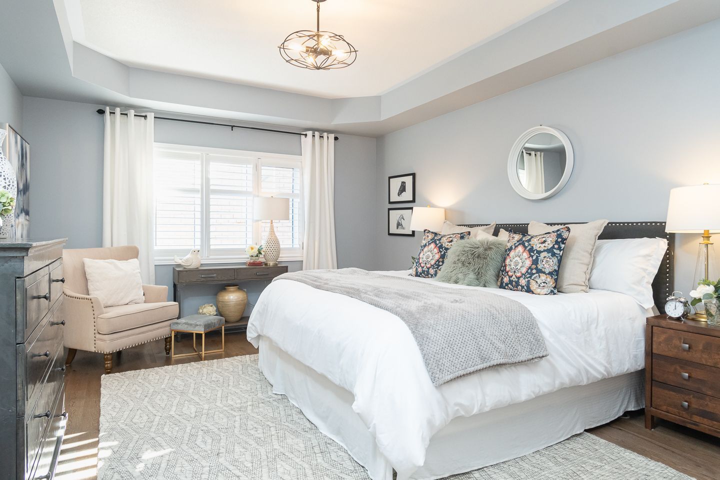 Bright bedroom with a white bed, gray walls, window seat, and wooden nightstand with lamp.