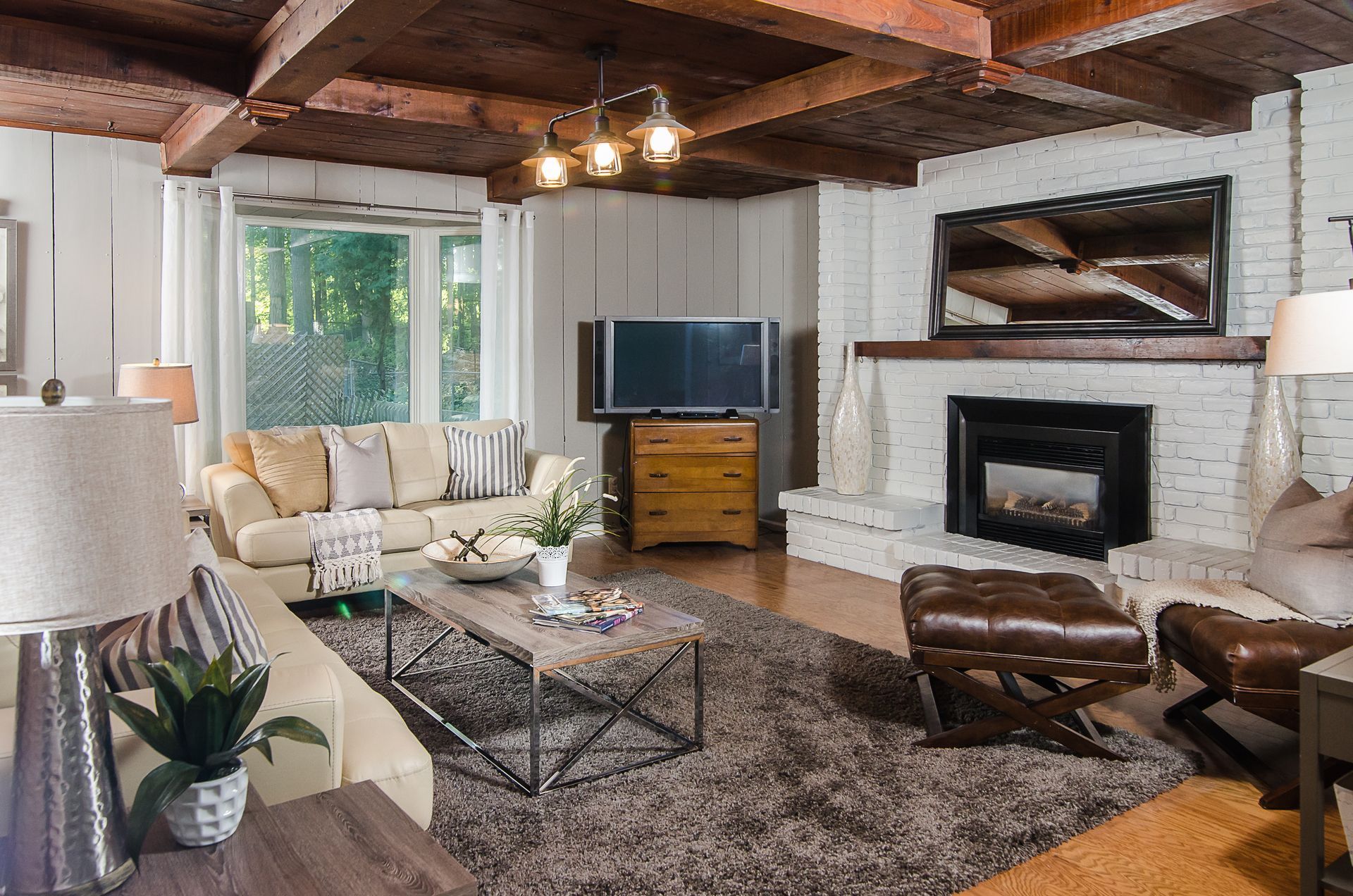 Cozy living room with exposed beams, cream sofas, TV, fireplace, and large windows