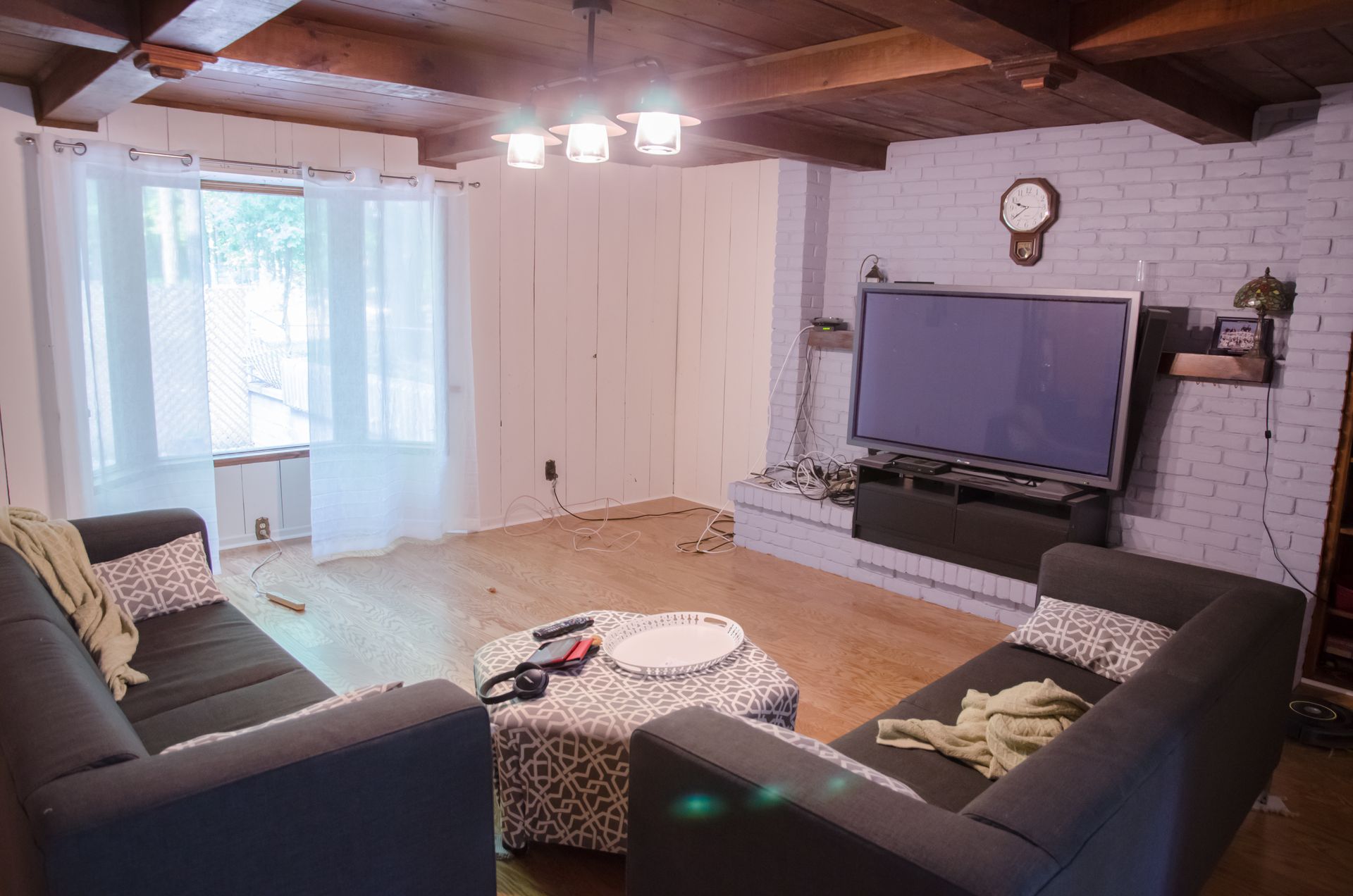 Cozy living room with dark sofas, large TV, white brick fireplace, and sliding glass doors with sheer curtains
