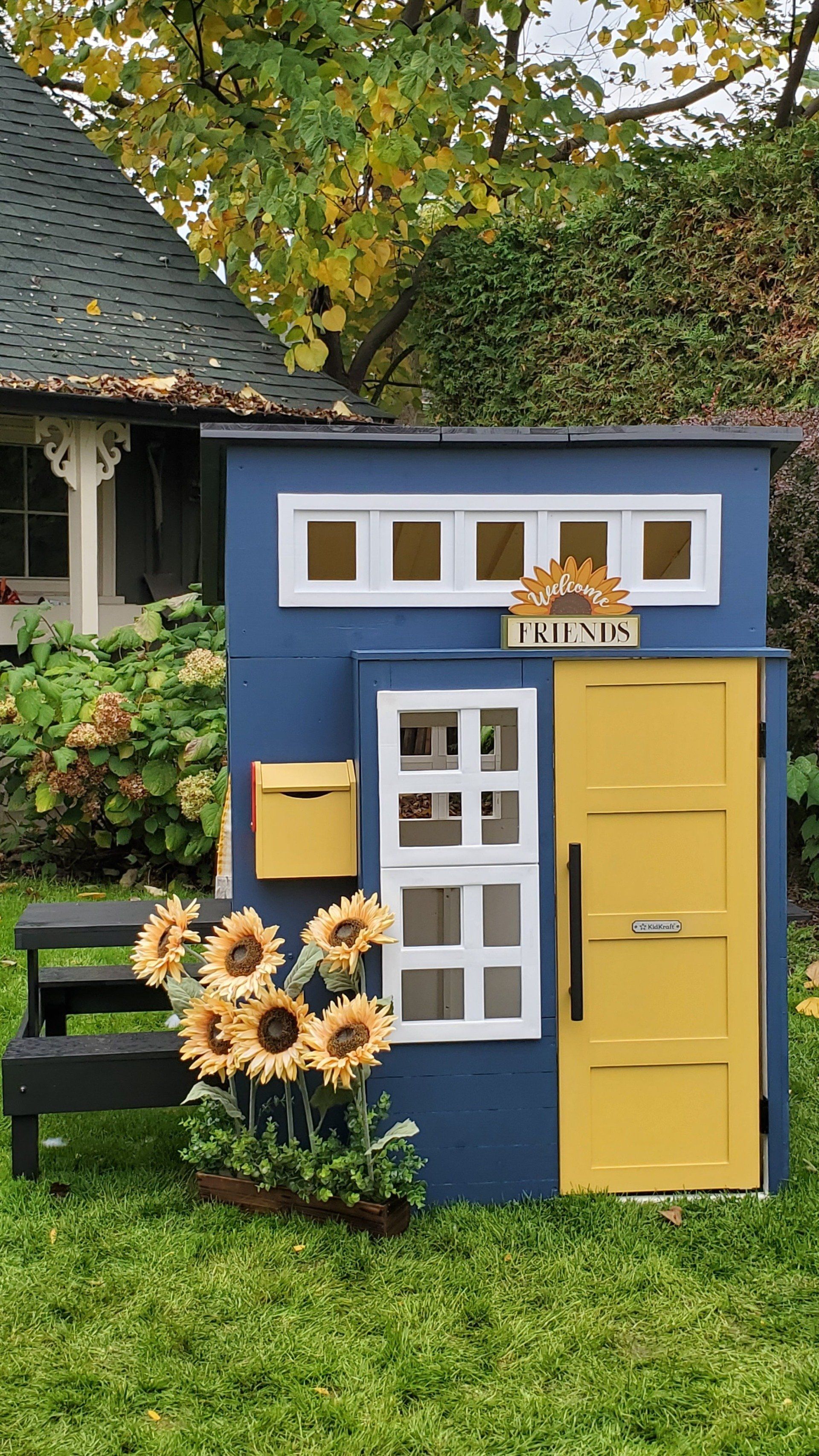 A blue and yellow playhouse is sitting in the grass in front of a house.