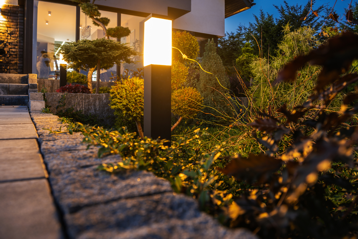 A lamp post in a garden next to a house at night.