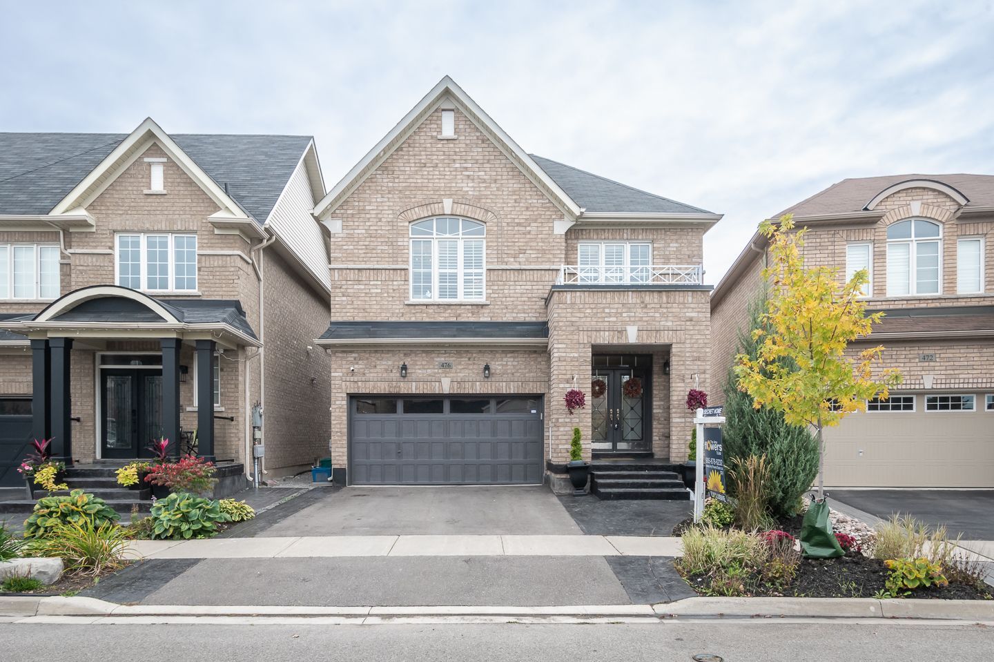 Row of modern brick suburban houses with driveways and garages, framed by landscaped front yards