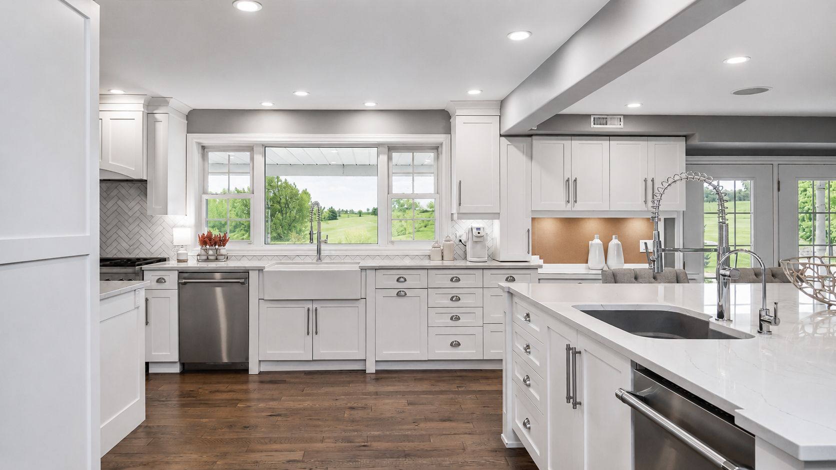 Bright modern white kitchen with island, stainless appliances, and large window overlooking greenery