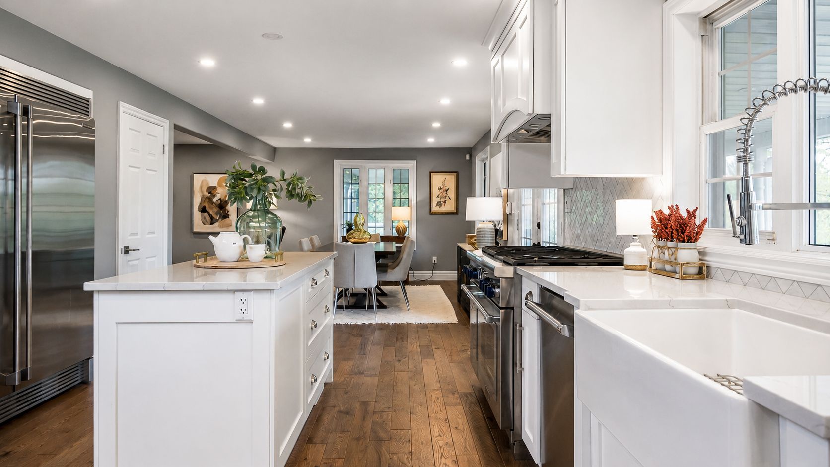 Bright modern kitchen with white cabinets, island, stainless appliances, and hardwood floors leading to a dining area