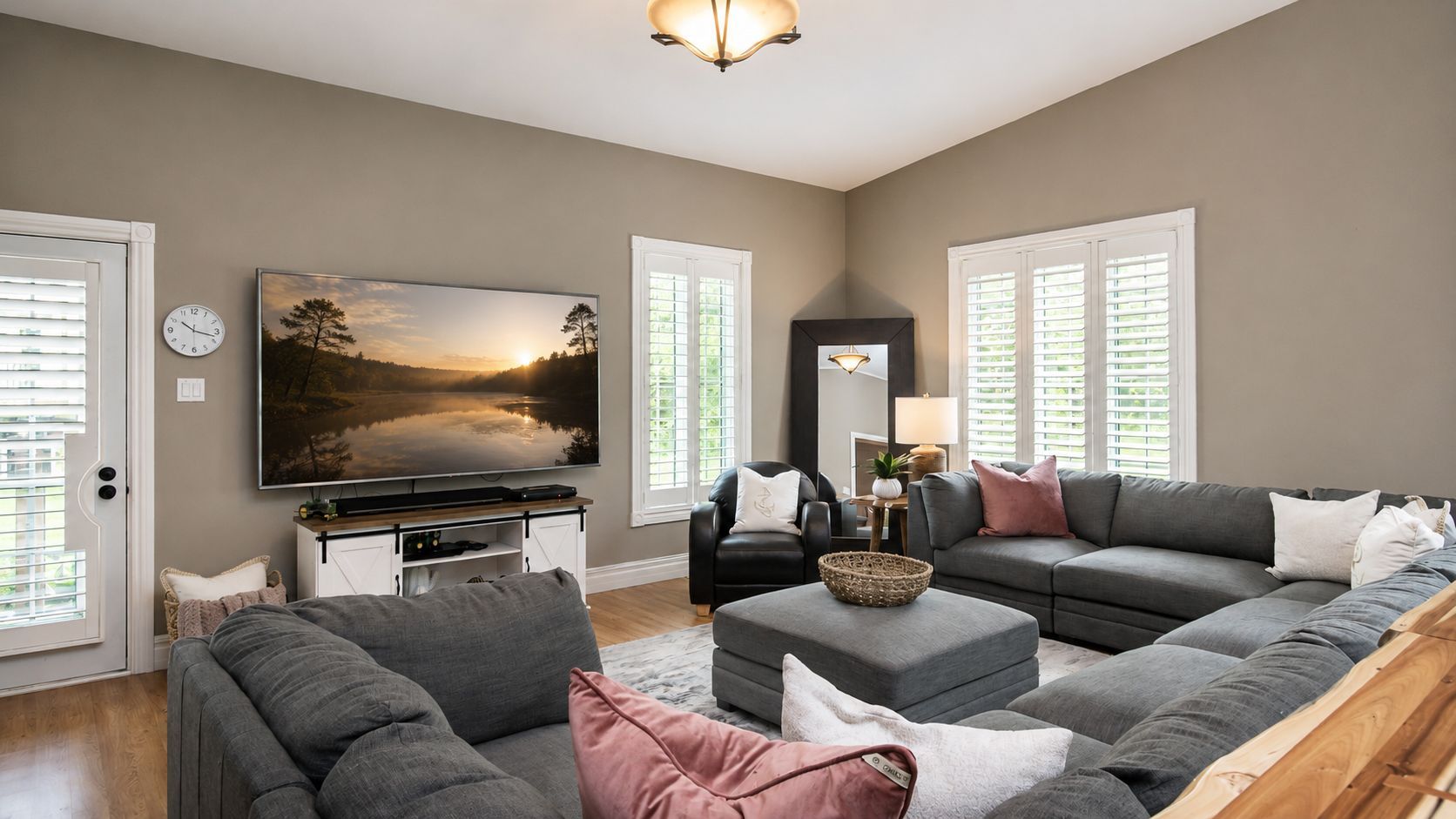 Modern living room with gray sectional, wall-mounted TV, white shutters, and neutral decor