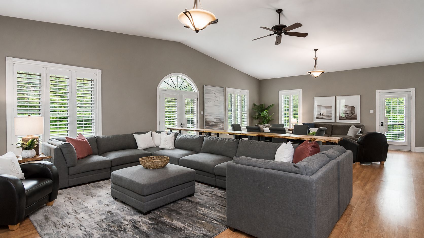 Spacious modern living room with gray sectional sofa, ottoman, hardwood floors, and large windows.