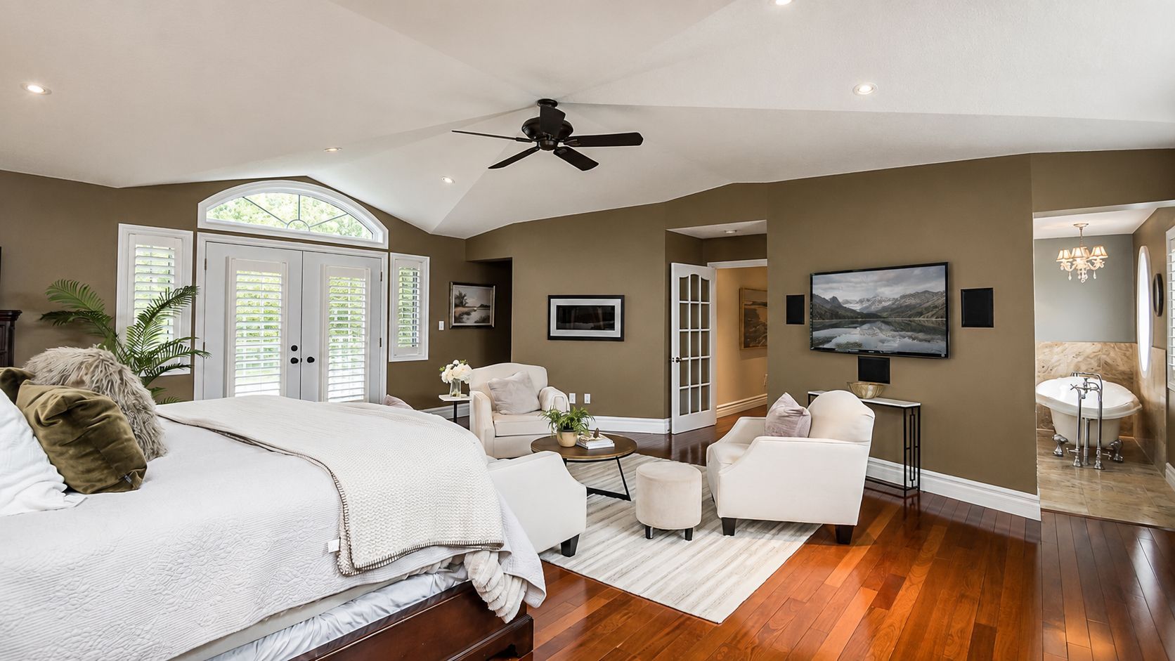 Spacious bedroom with white bedding, hardwood floors, fireplace, TV, and French doors to a balcony