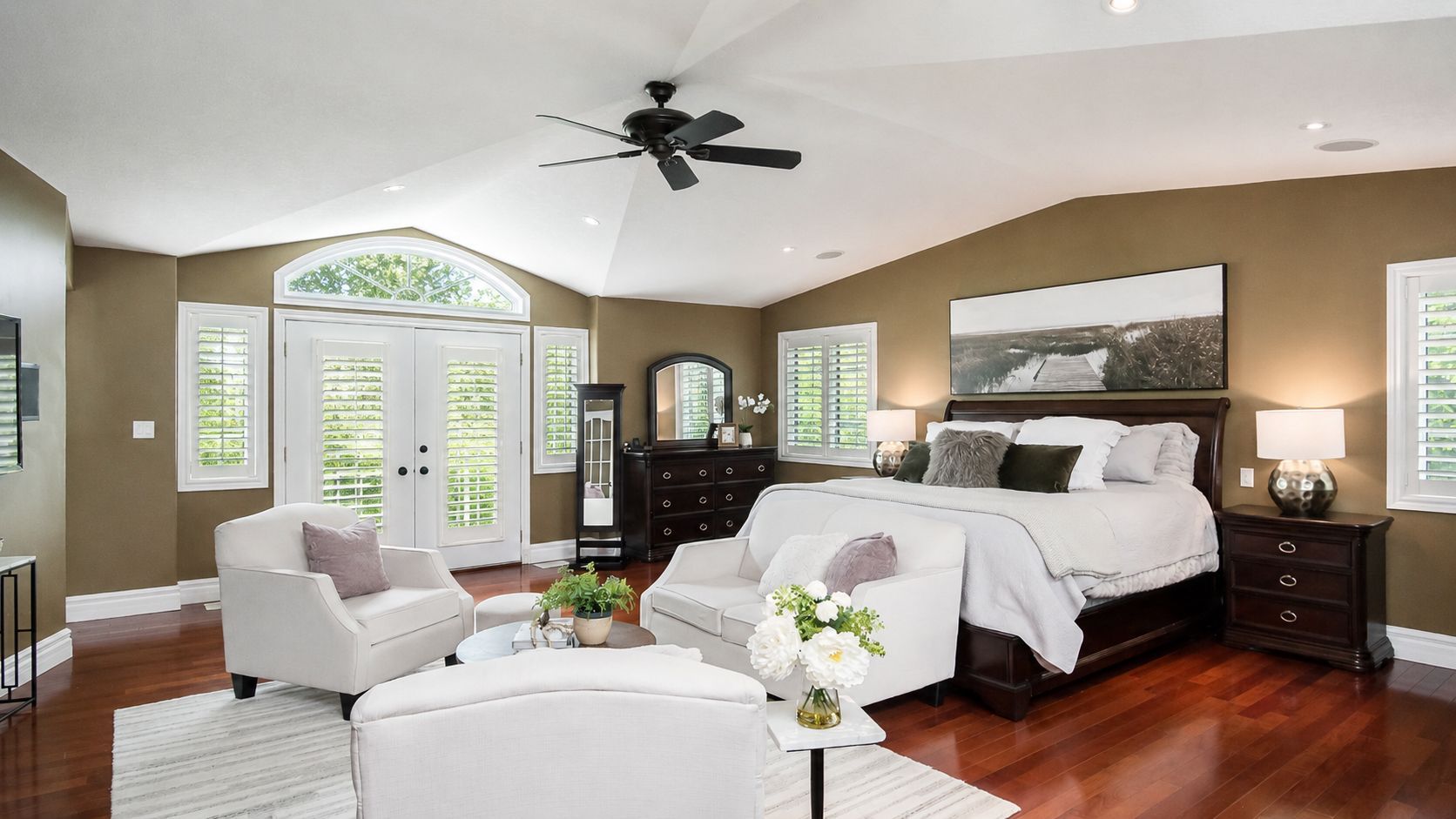 Bright bedroom with a large bed, white seating, hardwood floors, and French doors to a balcony.