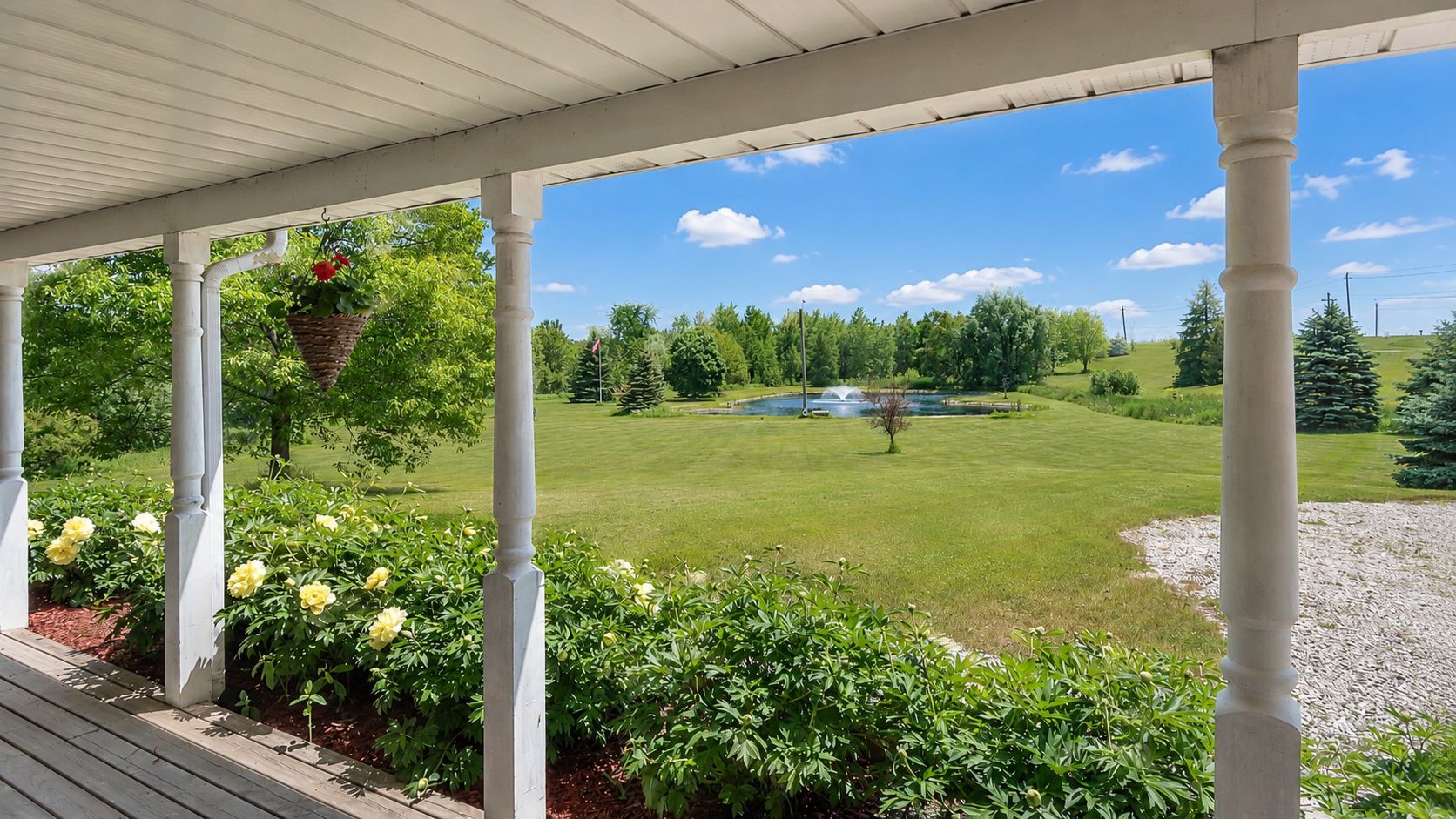 Porch view of a green lawn, pond, and trees under a bright blue sky