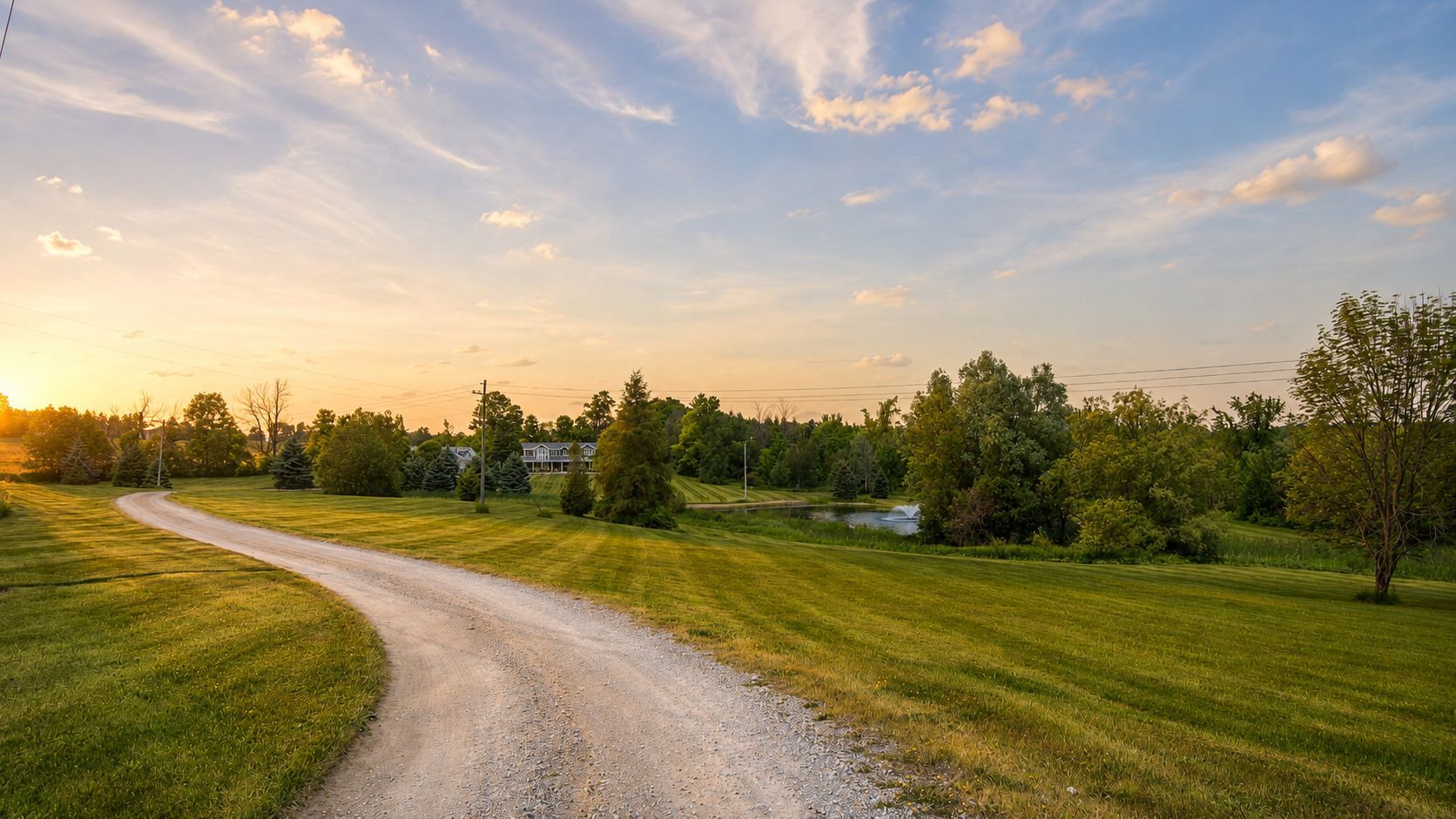 Curving gravel path through green fields at sunset under a colorful cloudy sky