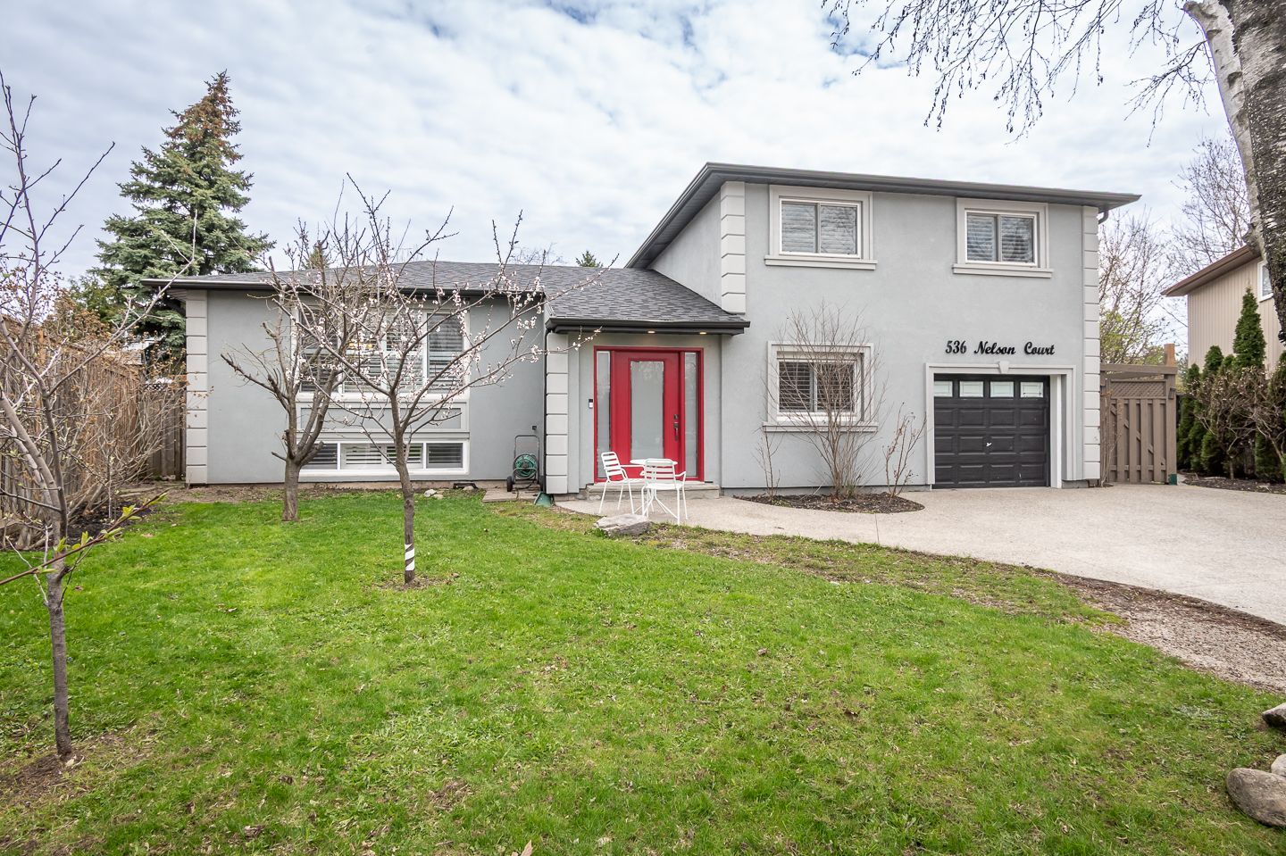 Two-story gray house with red front door, black garage, and a green lawn