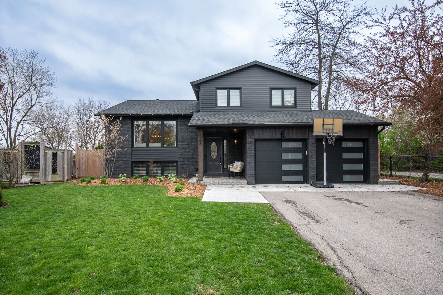Modern dark-gray two-story house with a large lawn and driveway under a blue sky