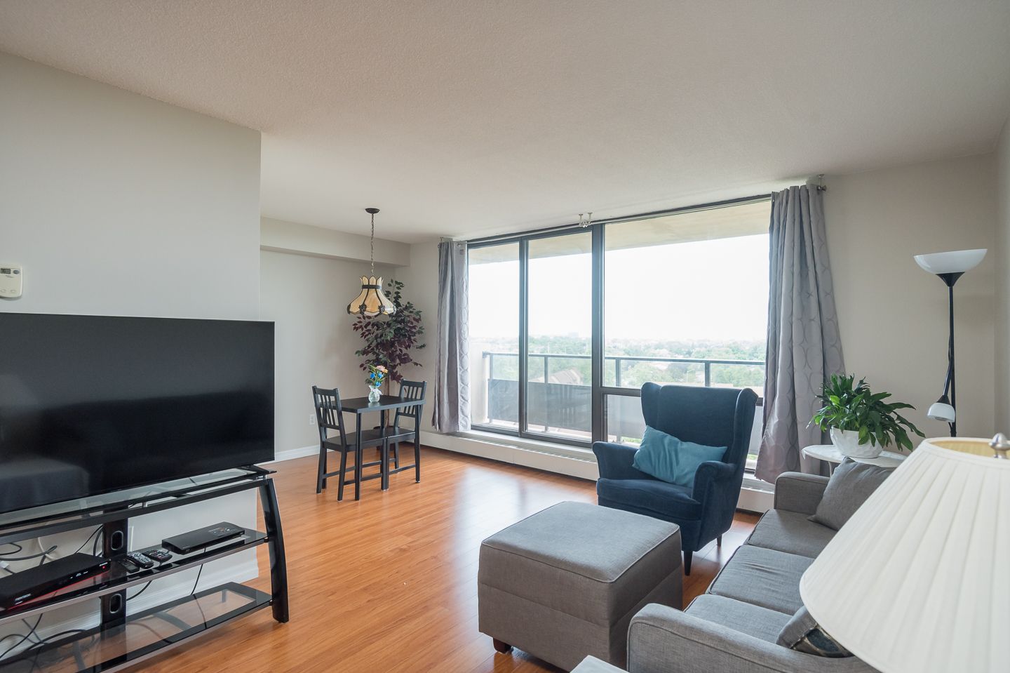 Bright living room with large windows, TV, gray ottoman, and blue armchair on hardwood floor