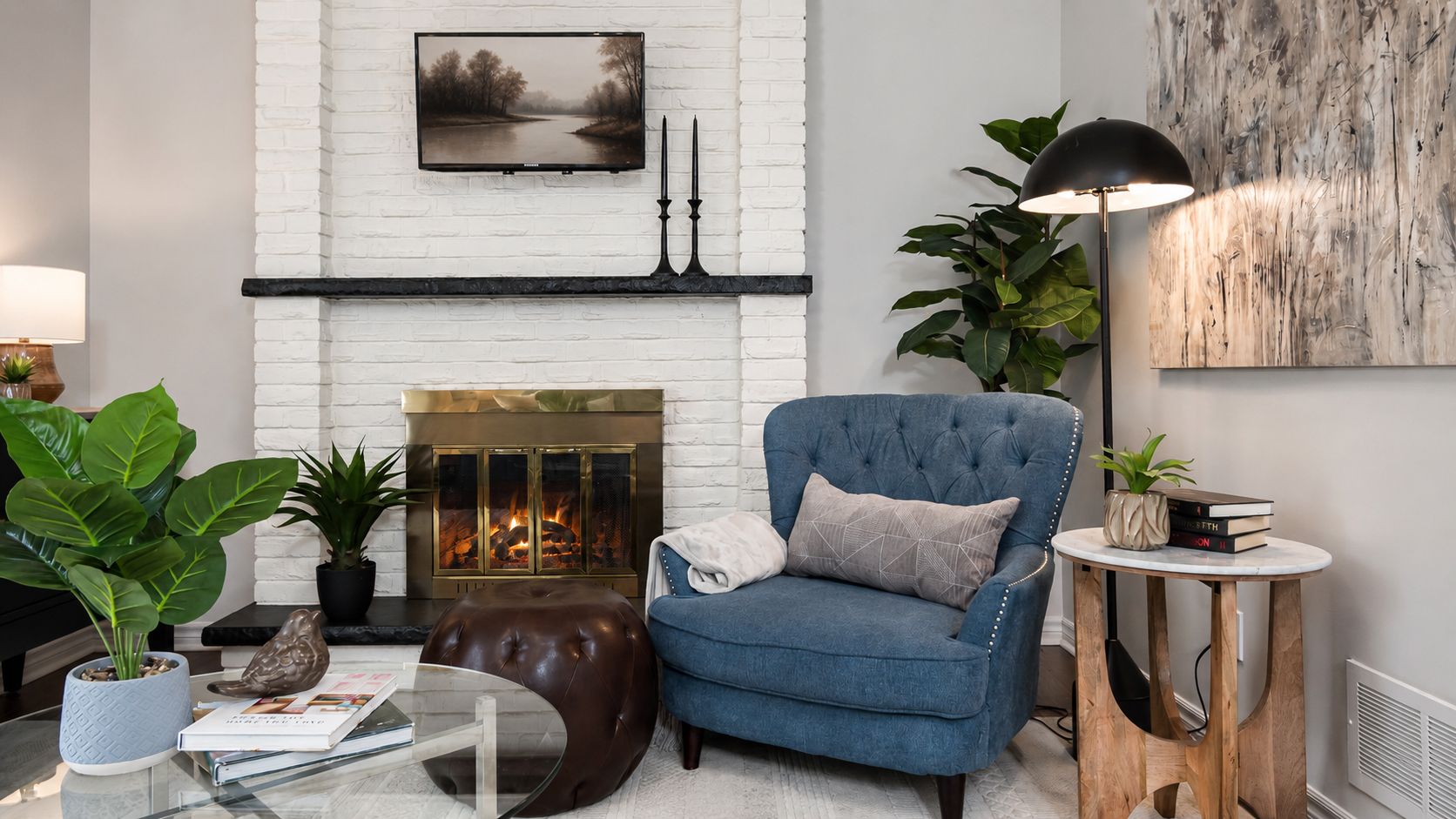 Cozy living room with blue armchair, white brick fireplace, floor lamp, and potted plant.