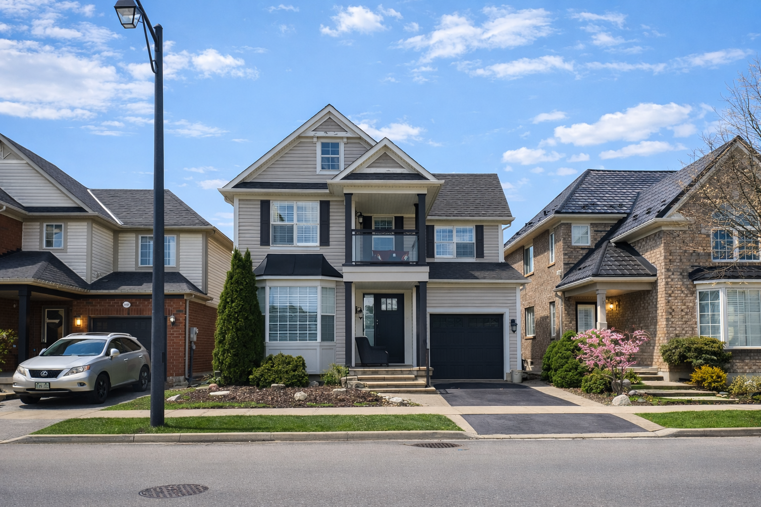 Suburban two-story house with gray siding, black garage door, and a parked car beside a streetlamp.