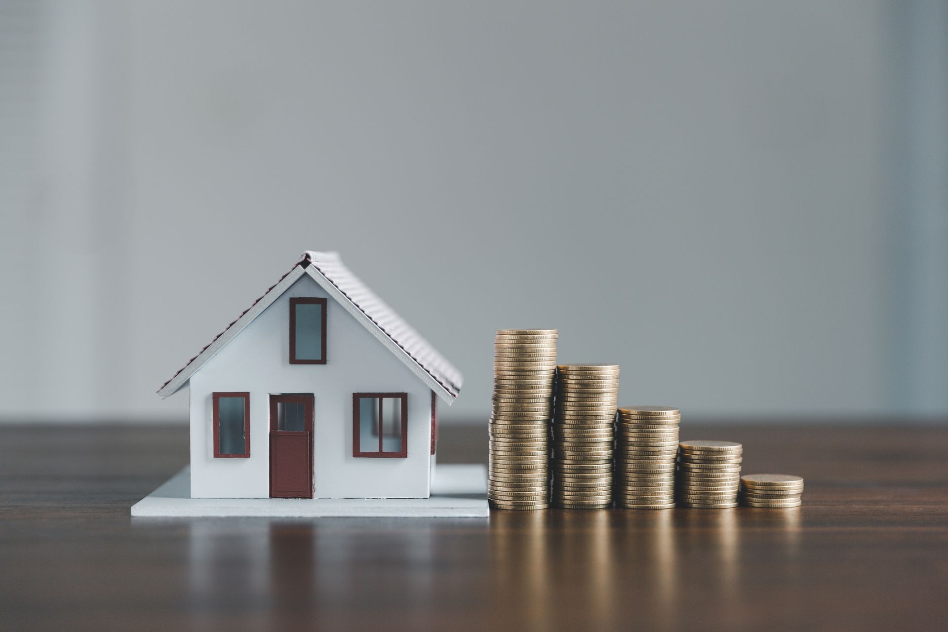 A model house is sitting next to stacks of coins on a table.