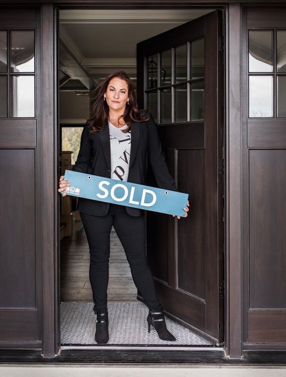 A woman is holding a sold sign in front of a door.