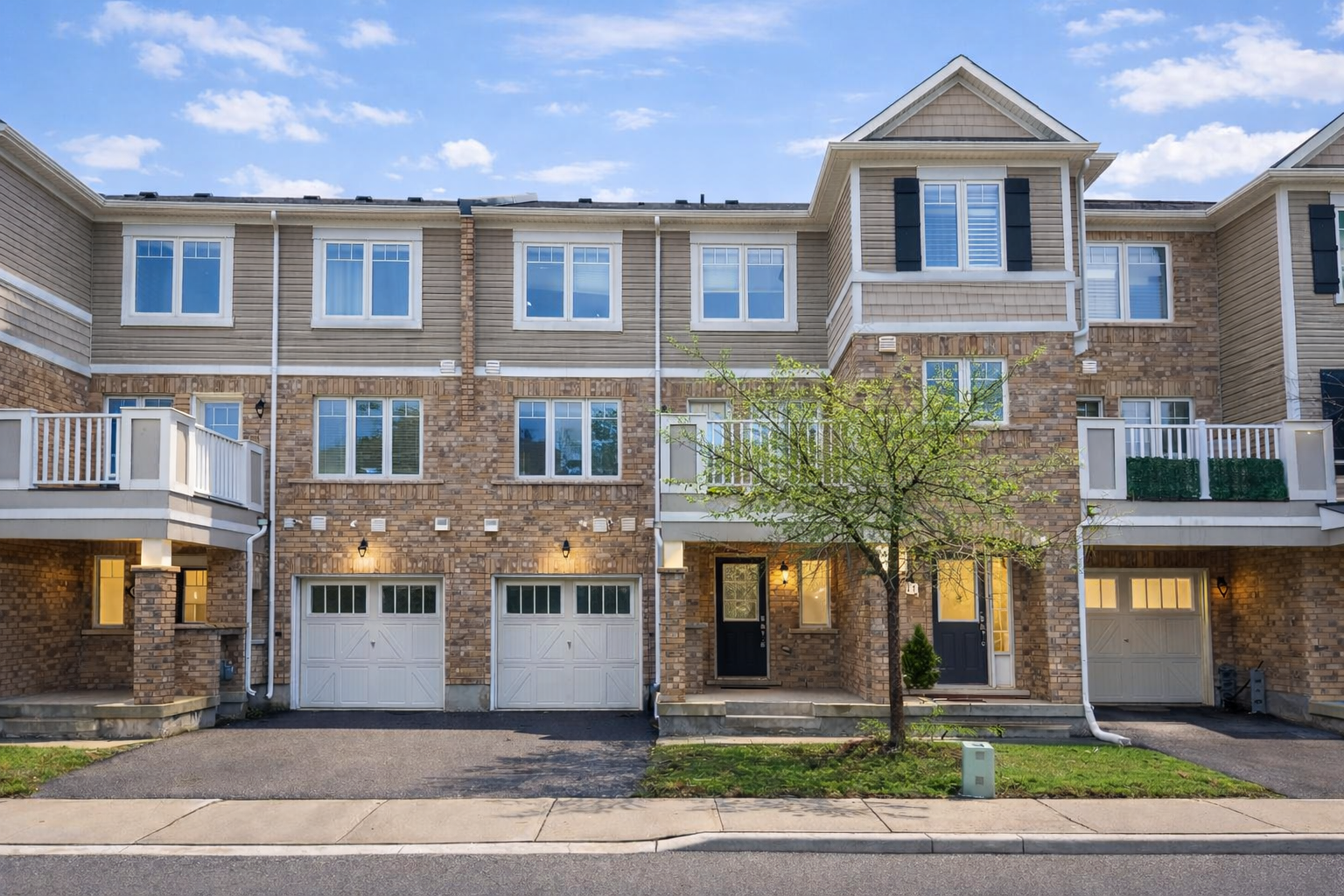 Modern brick townhouse row with balconies, garages, and a tree-lined street in front