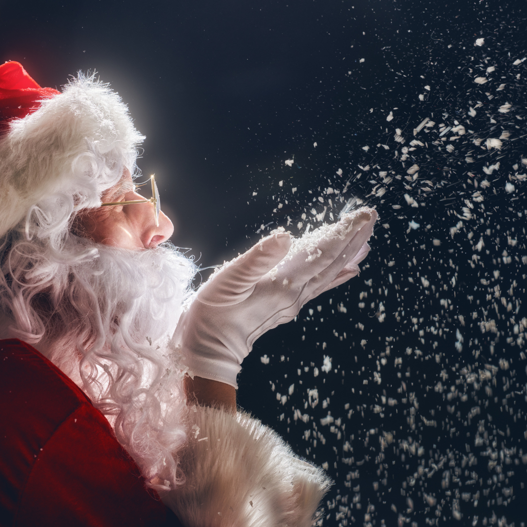 Santa Claus blowing snow, wearing red suit and hat, white beard and gloves, dark background.