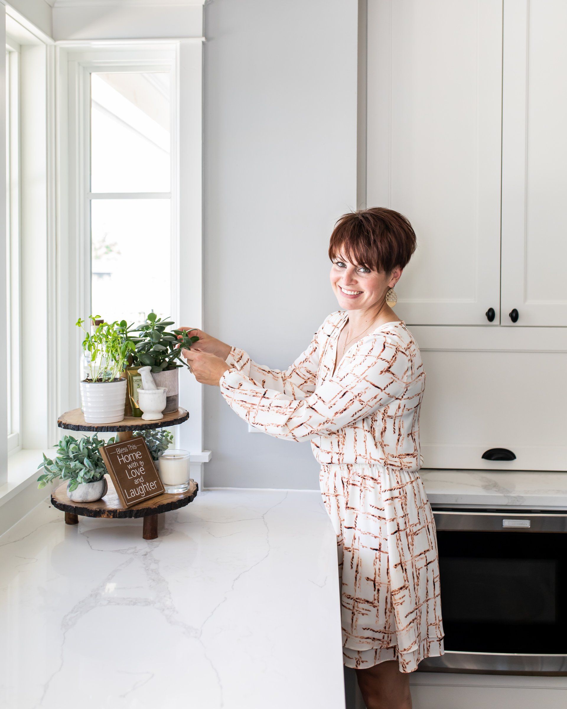 A woman is standing in a kitchen arranging potted plants on a shelf.