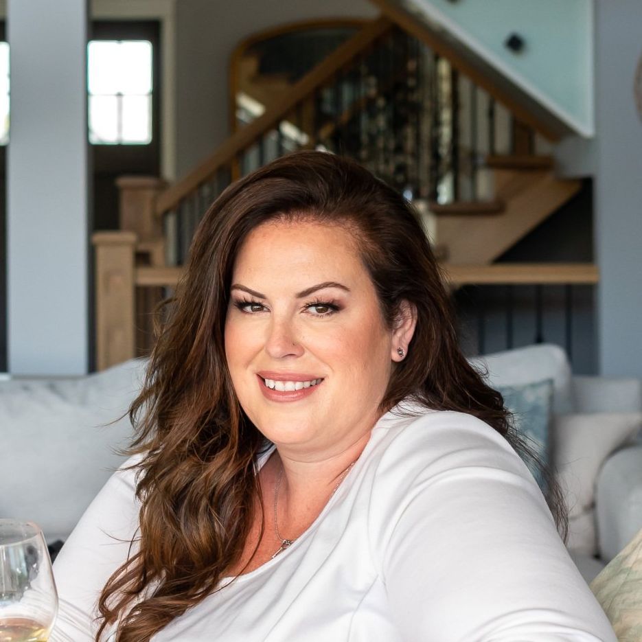 A woman is sitting on a couch in a living room with a glass of wine.