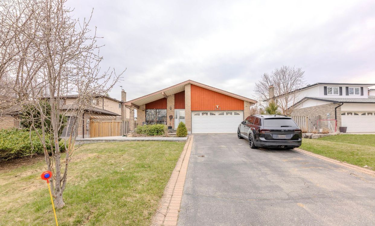 Suburban house with orange gable, driveway, parked black SUV, and leafless trees on a cloudy day